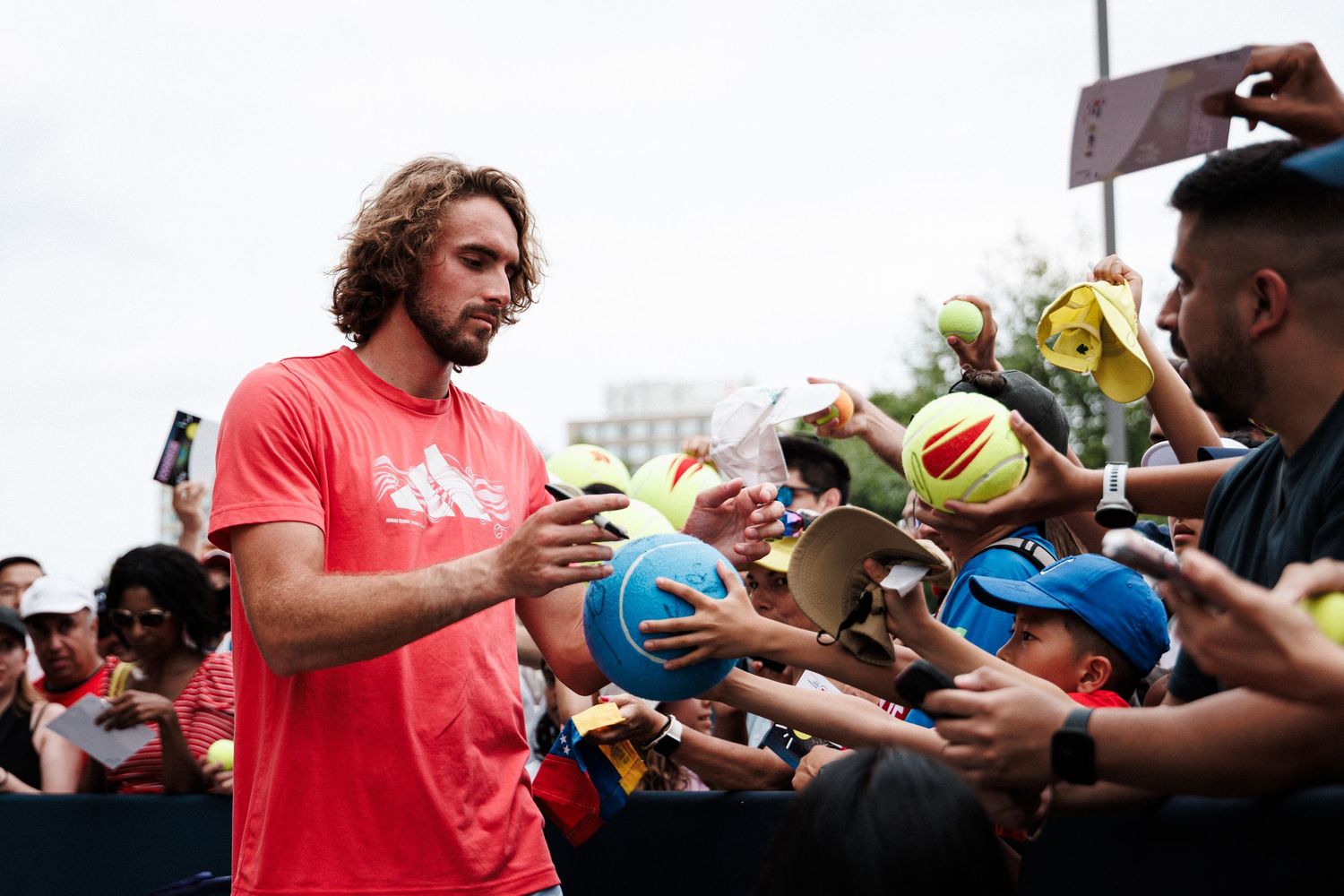 Athletes sign autographs and interact with fans at a sports event, wearing red jerseys and engaging with the crowd.