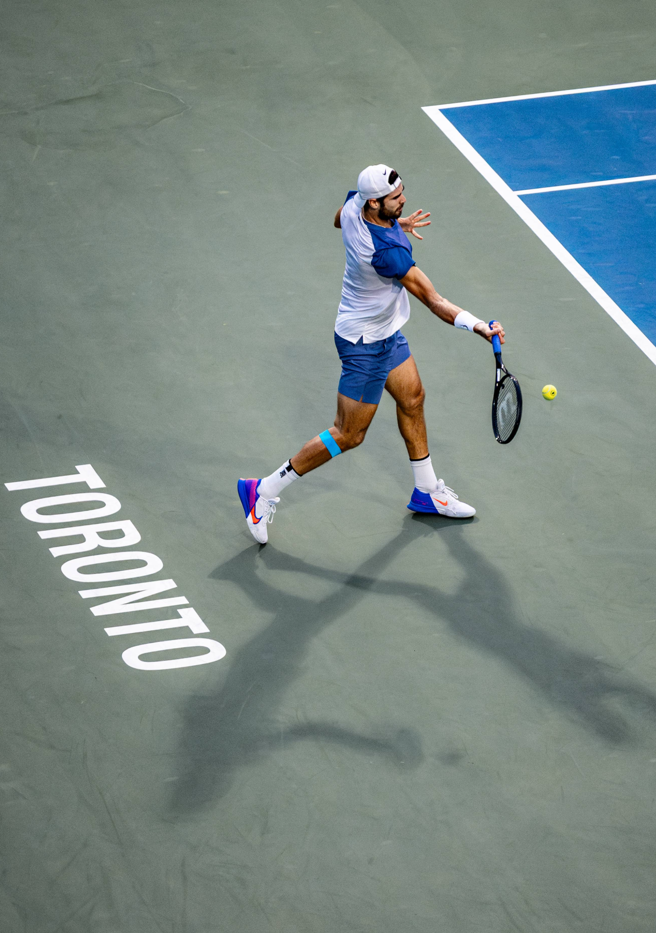 Tennis player in blue athletic wear stretches low to return a shot on a hard court during a match.