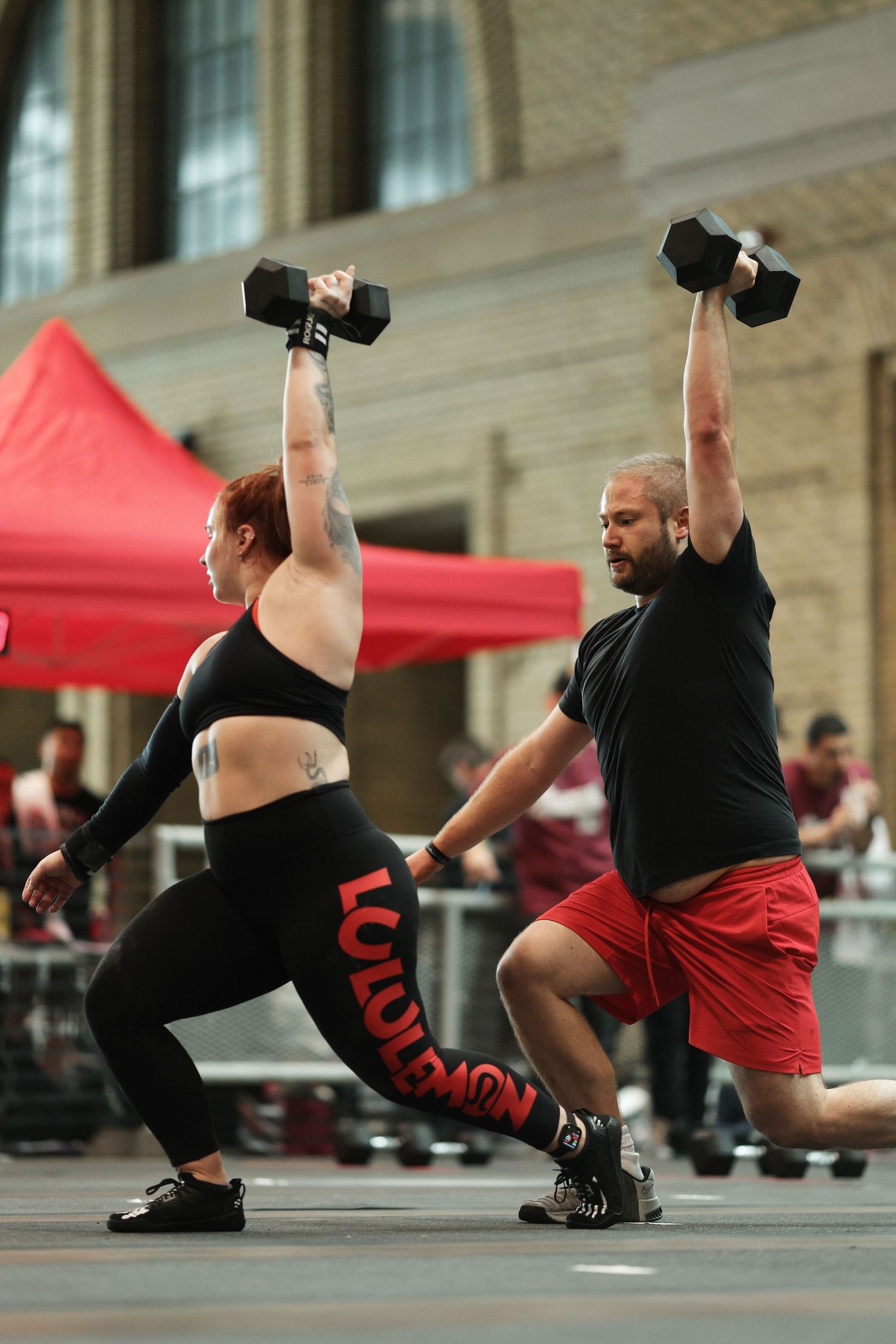 A sequence of dancers performing synchronized movements with dumbbells on the ground in black and red outfits.