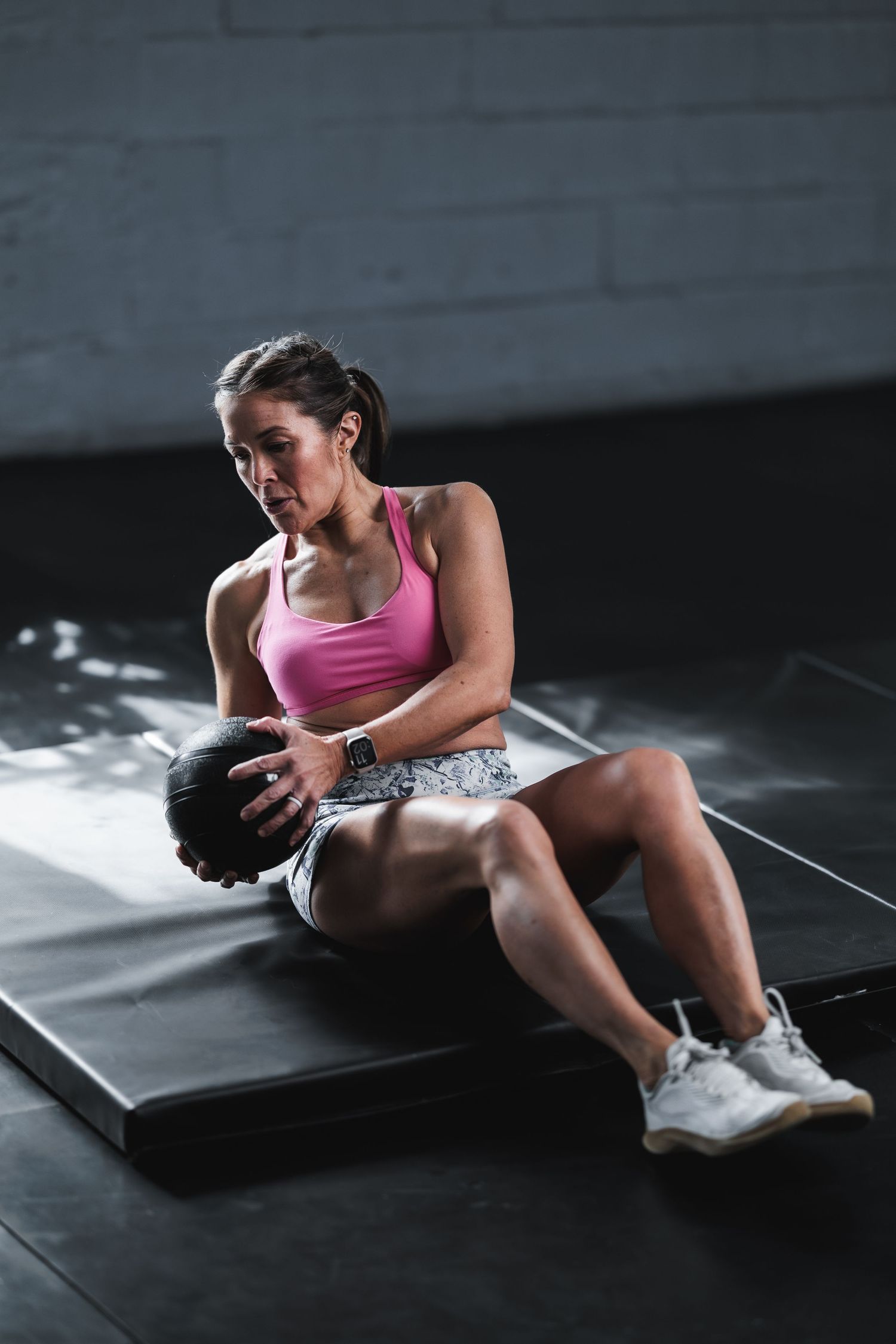 Athlete in pink top performing core exercises with a medicine ball on a gym mat.