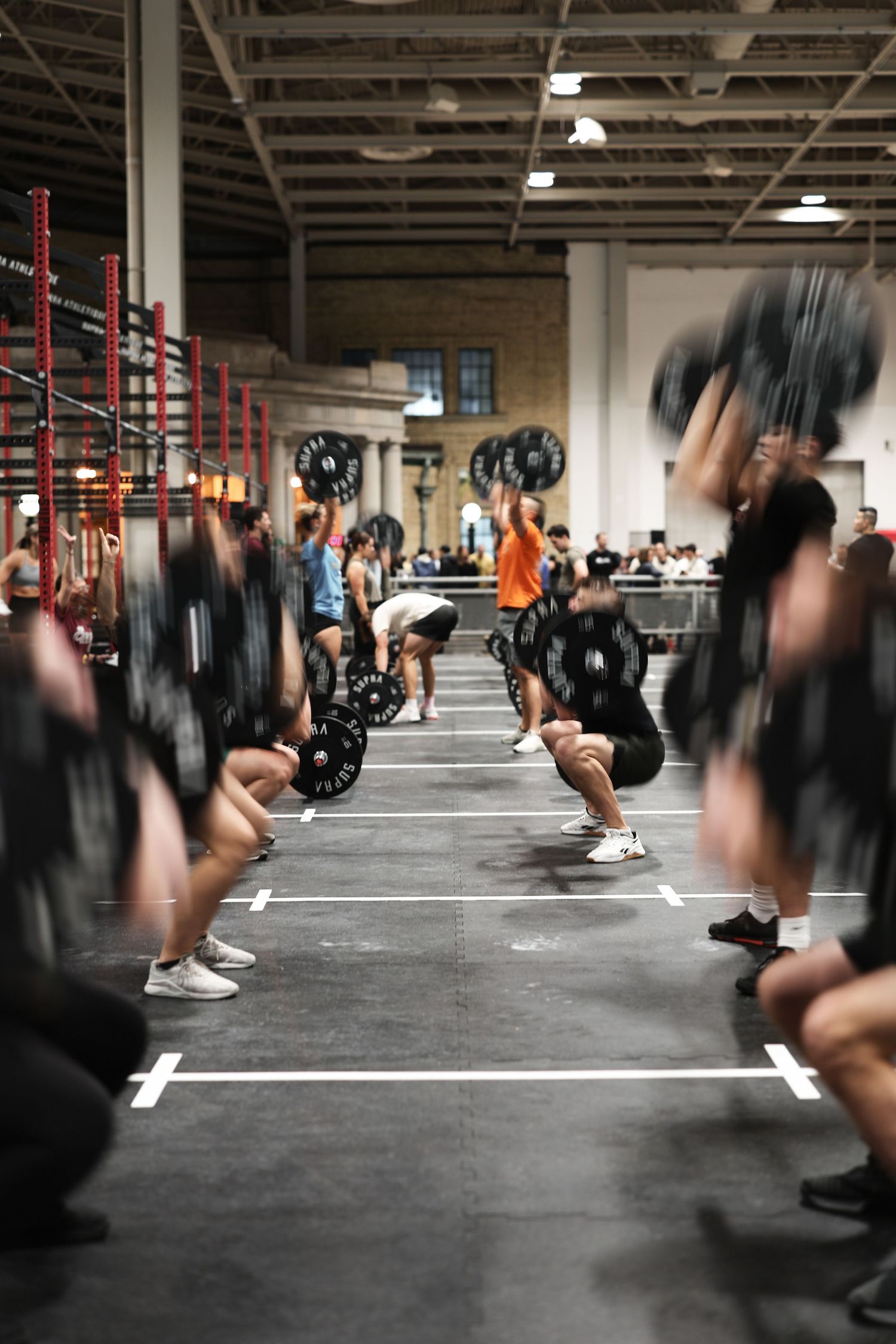Group of athletes performing synchronized barbell exercises in a spacious CrossFit gym during training session.