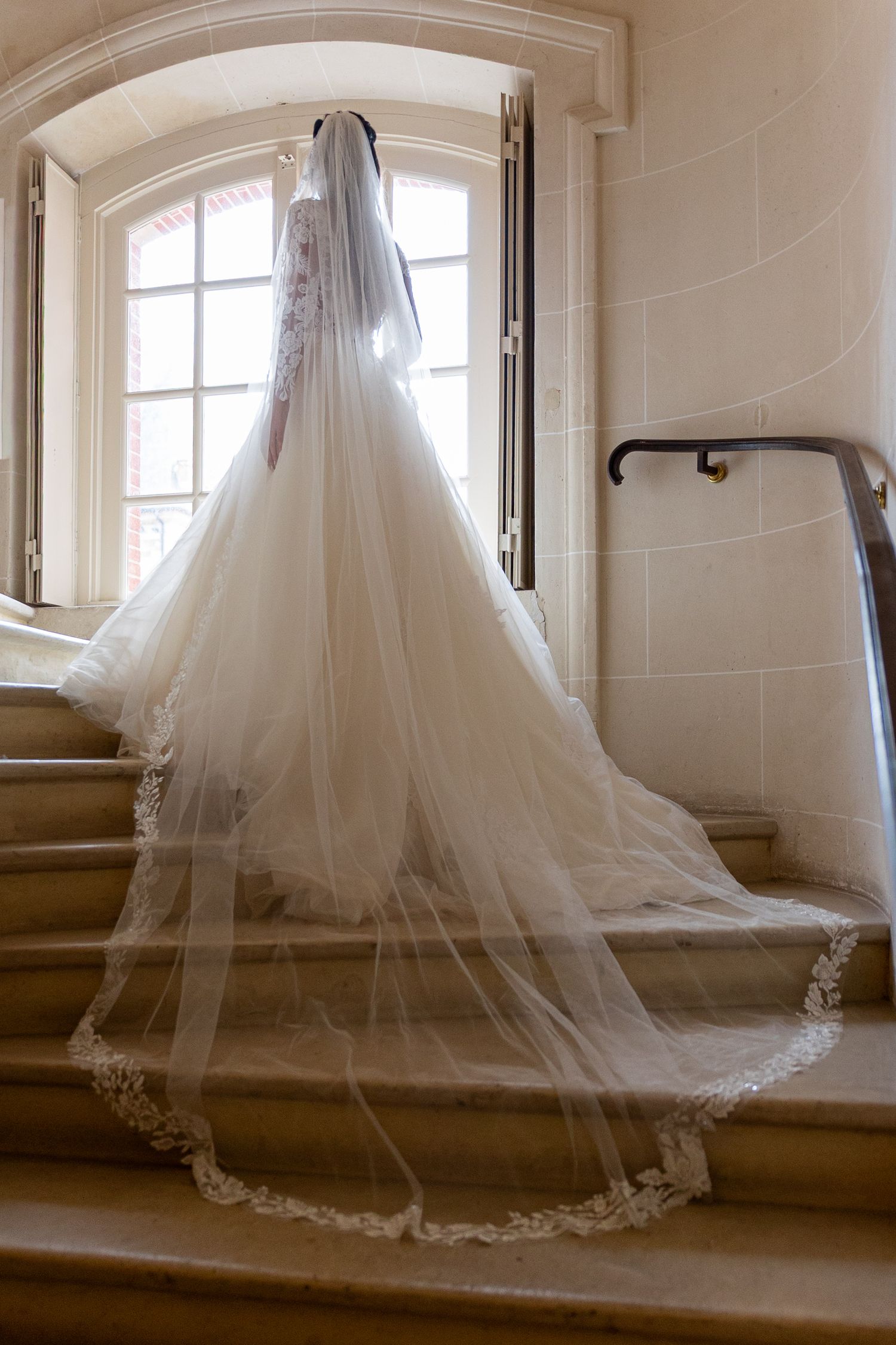 Long flowing white wedding dress train with delicate lace details displayed against a window backdrop.
