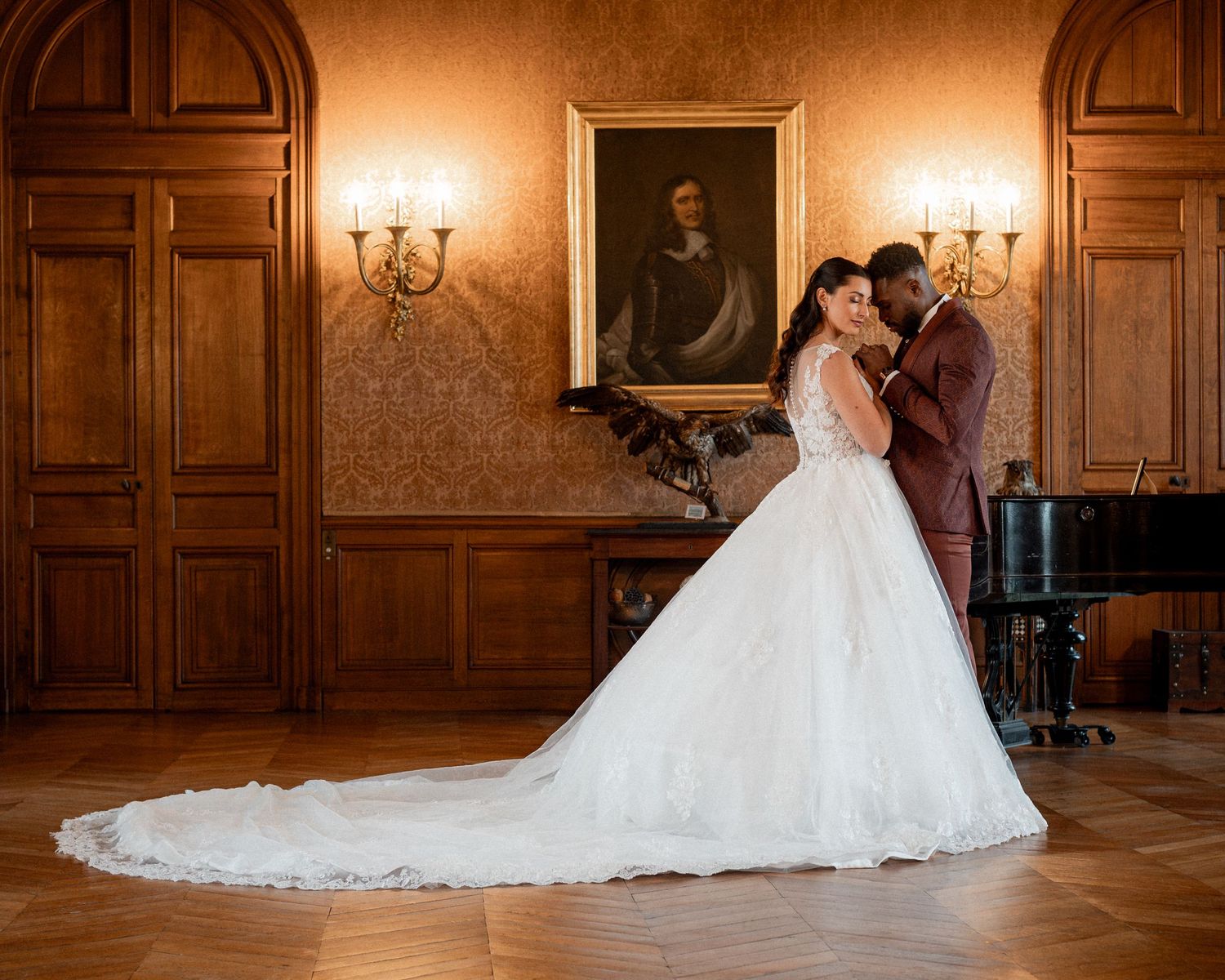 Elegant bride and groom share a romantic moment in a grand ballroom with wood paneling and classic portrait.
