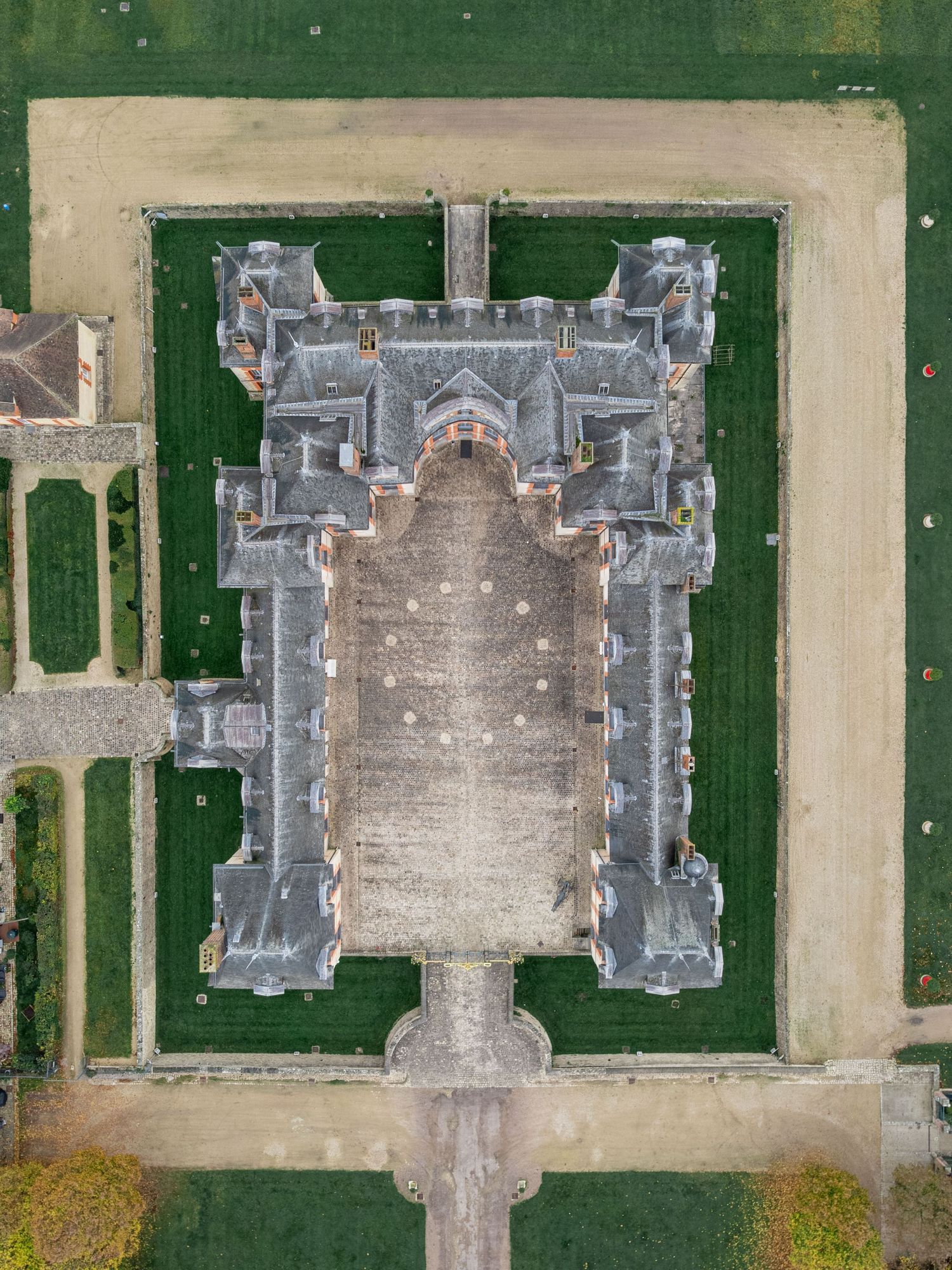 Aerial view of a historic stone castle complex with symmetrical architecture and green lawns.