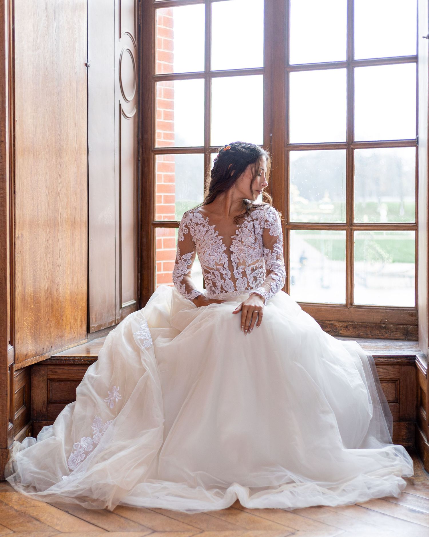 Dramatic full-length shot of a wedding gown with lace details against wooden window frames.