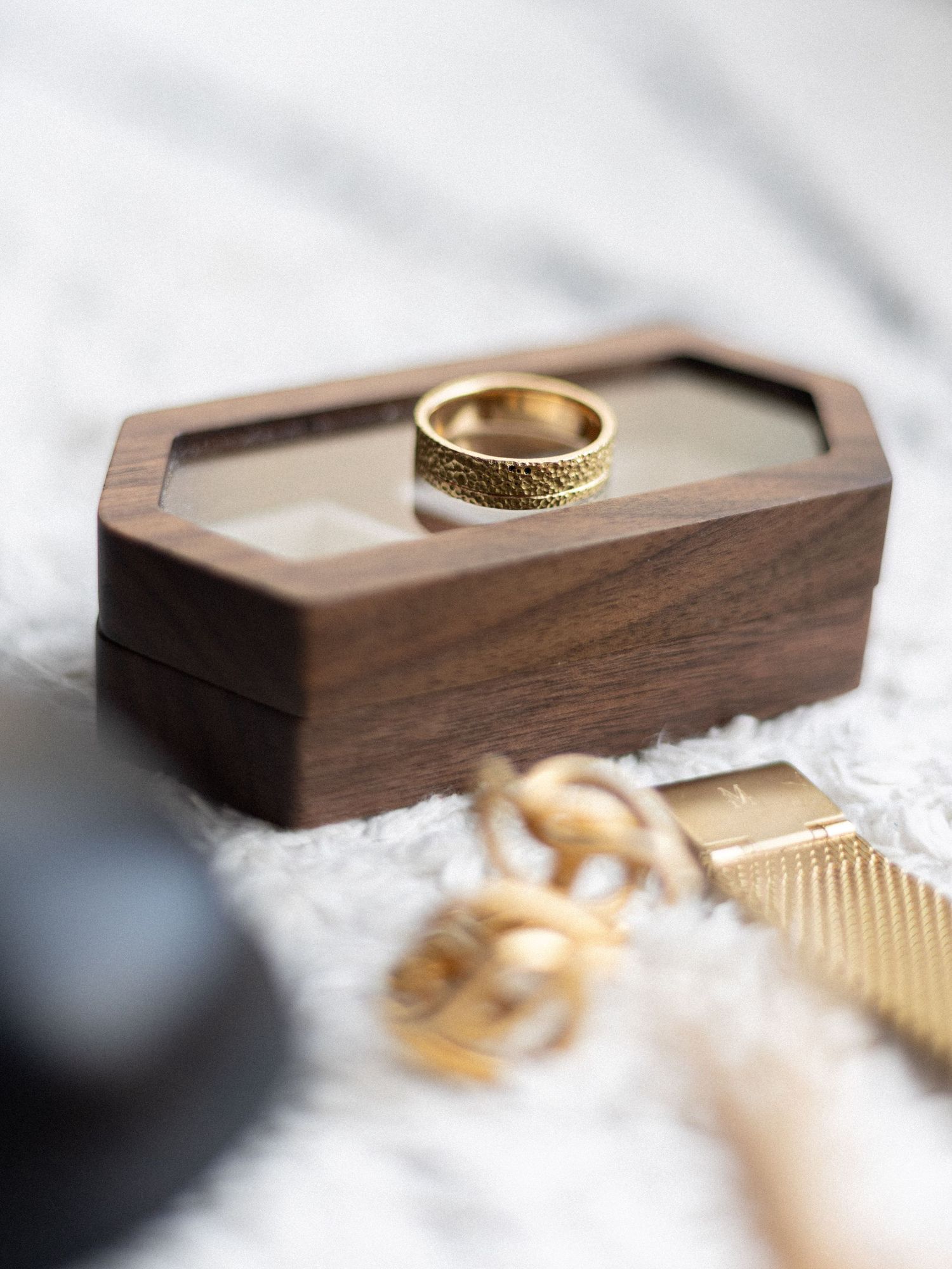 Gold wedding rings displayed in wooden ring box with delicate lace details.