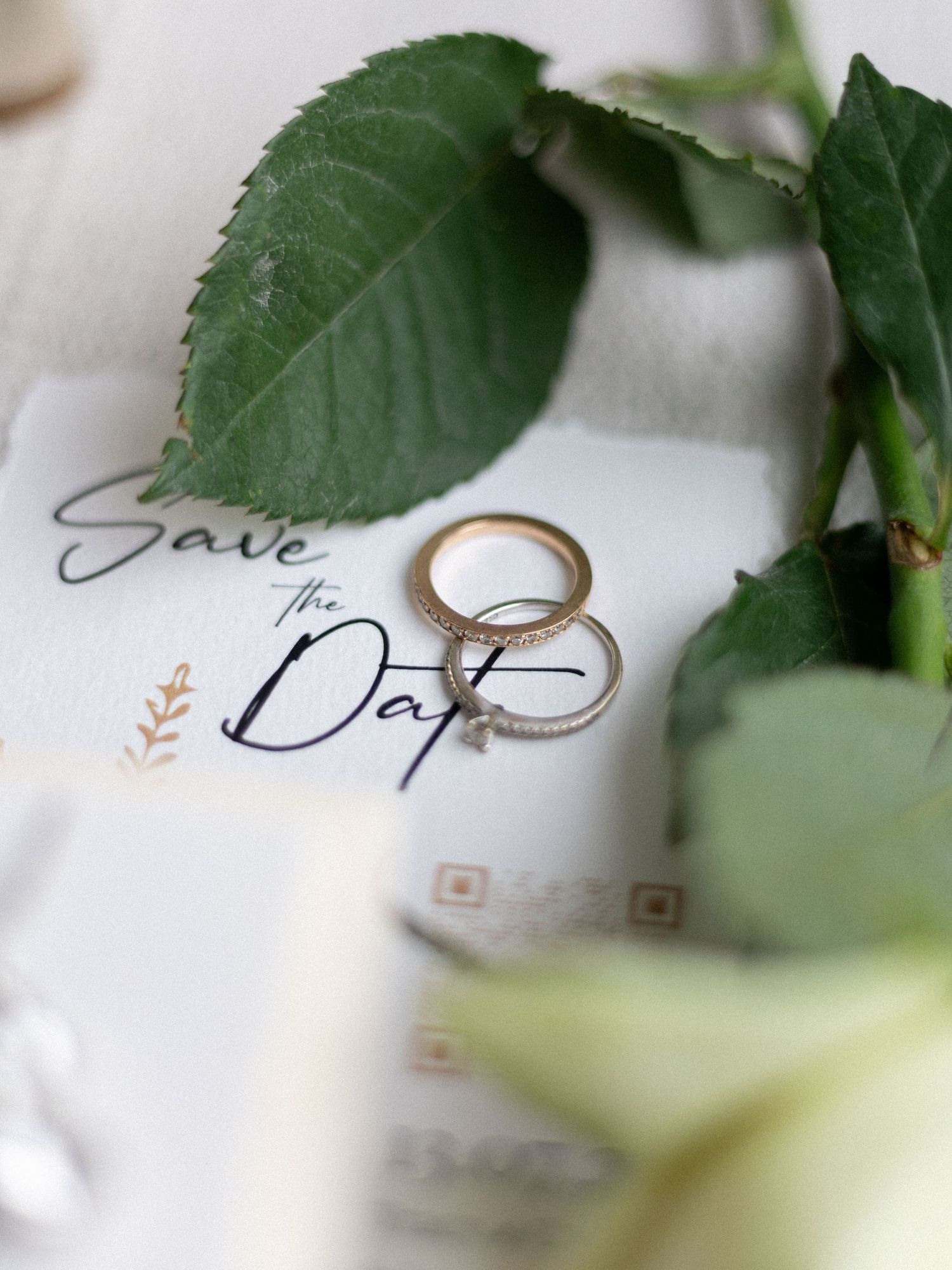 Close-up of wedding invitation with green foliage and gold rings.