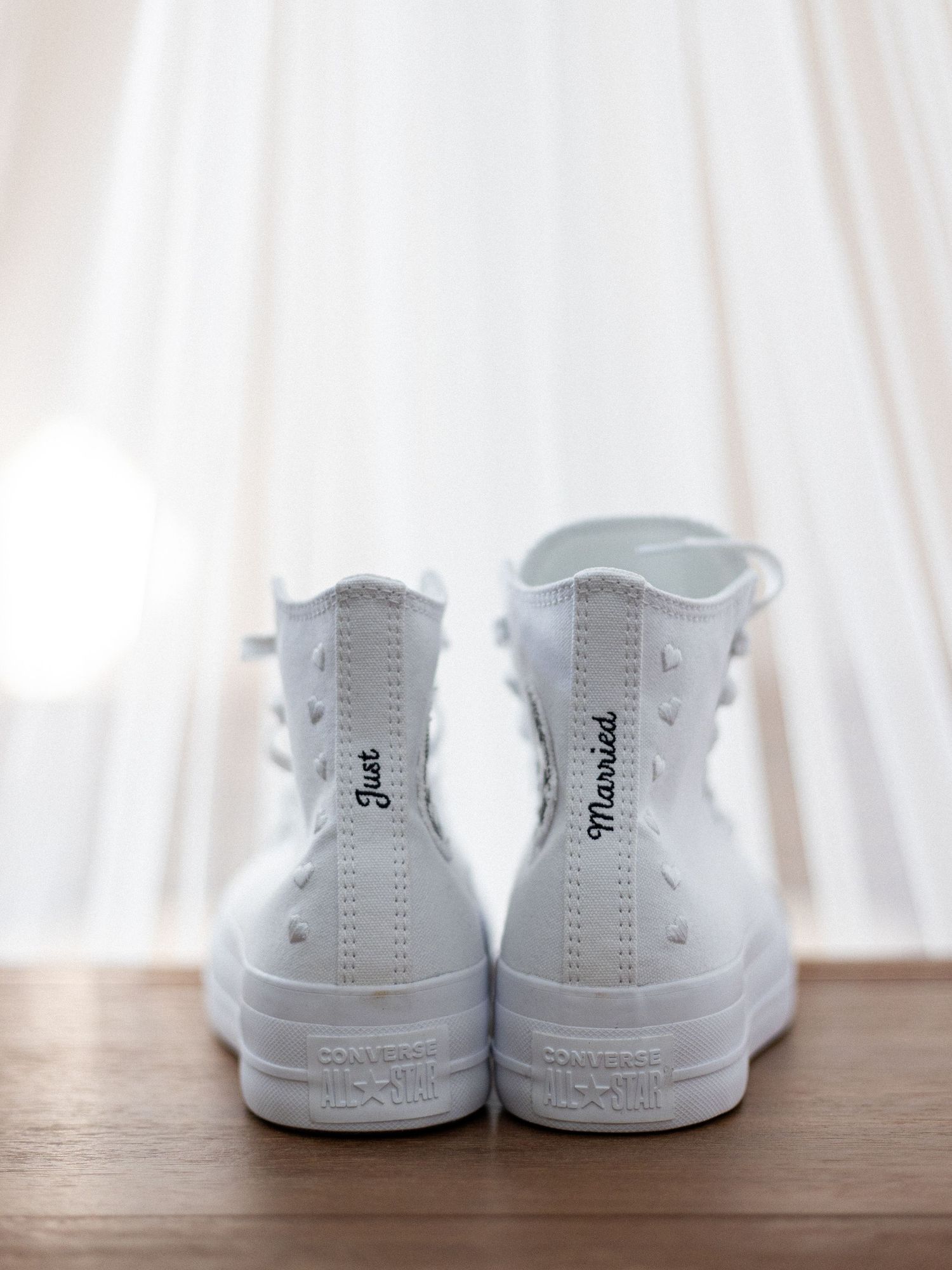 A pair of white high-top sneakers shown from behind on a wooden surface.