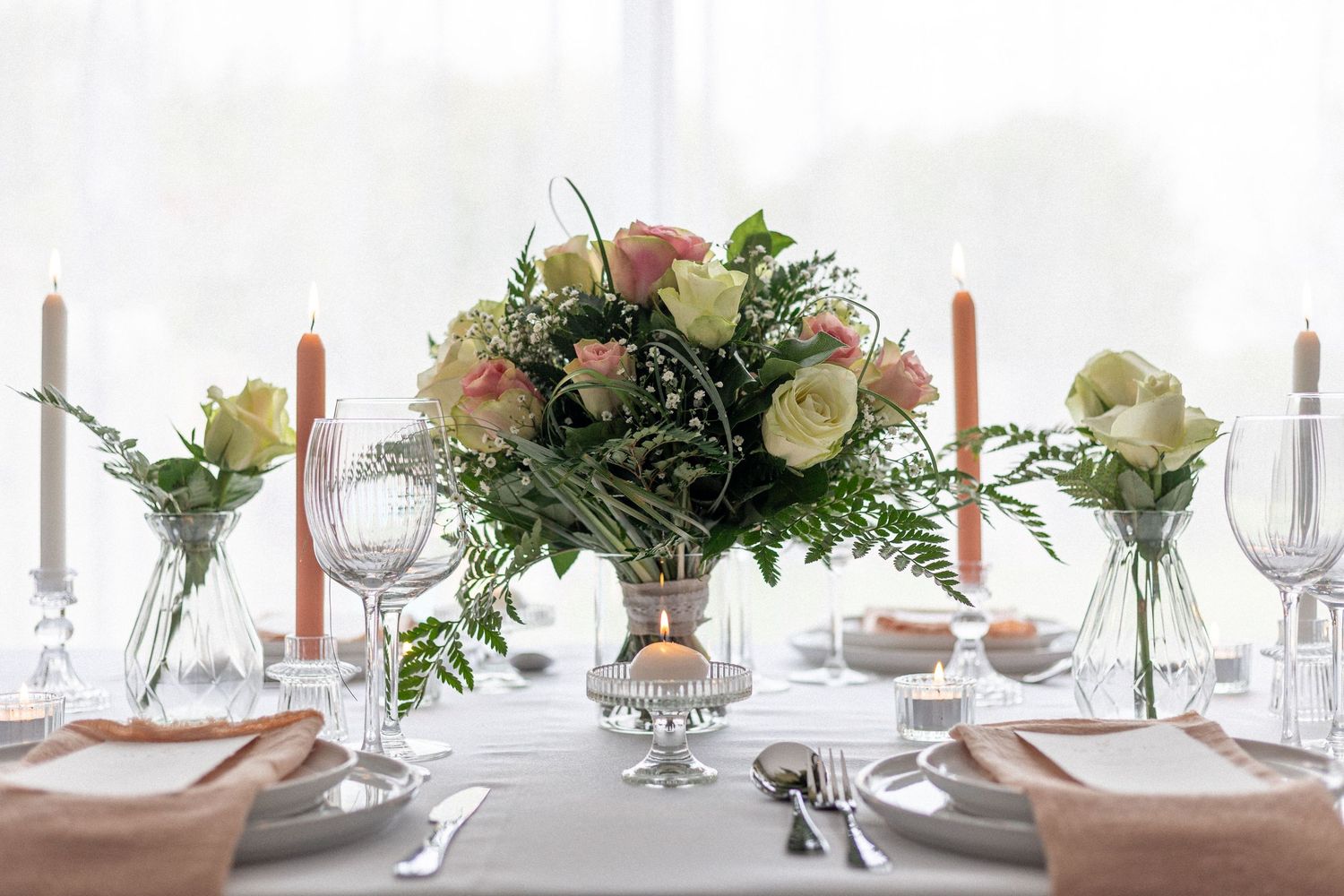 Long wedding reception table with elegant white and peach decor, candles, and floral arrangements.