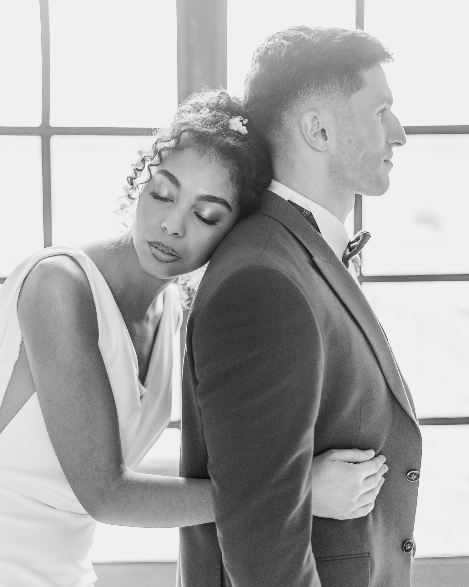 Intimate wedding couple portraits in soft window light against white backdrop.