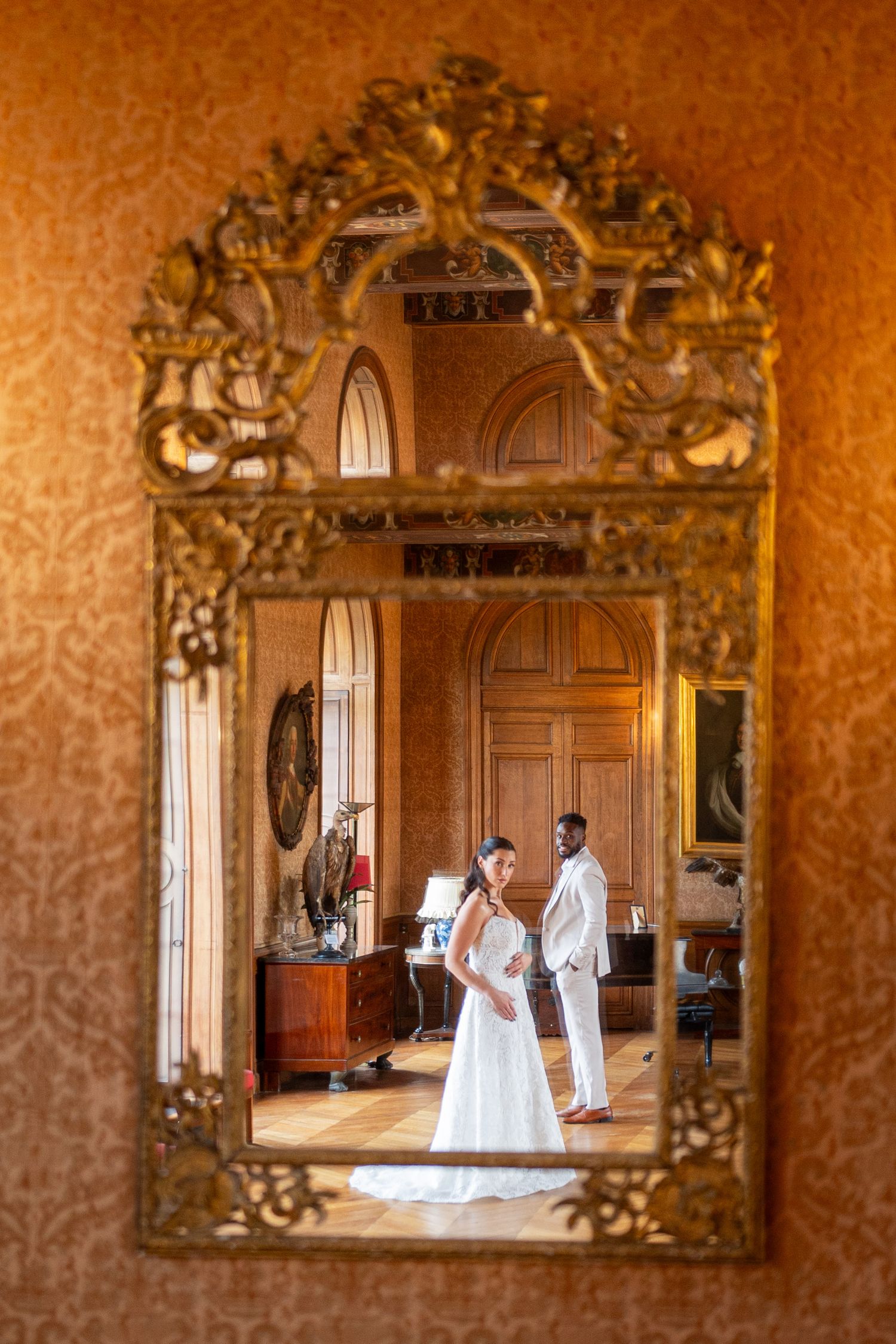 Wedding couple reflected in ornate gold mirrors during intimate indoor photo session.