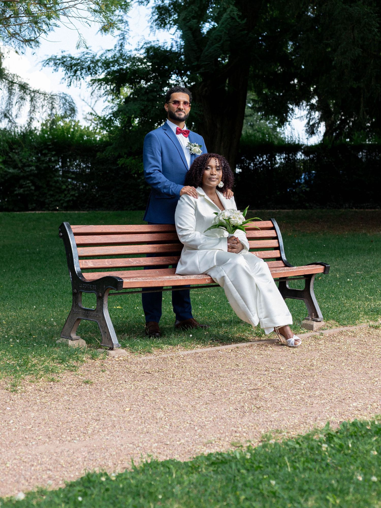 Couple sitting together on a wooden park bench surrounded by green trees and grass.