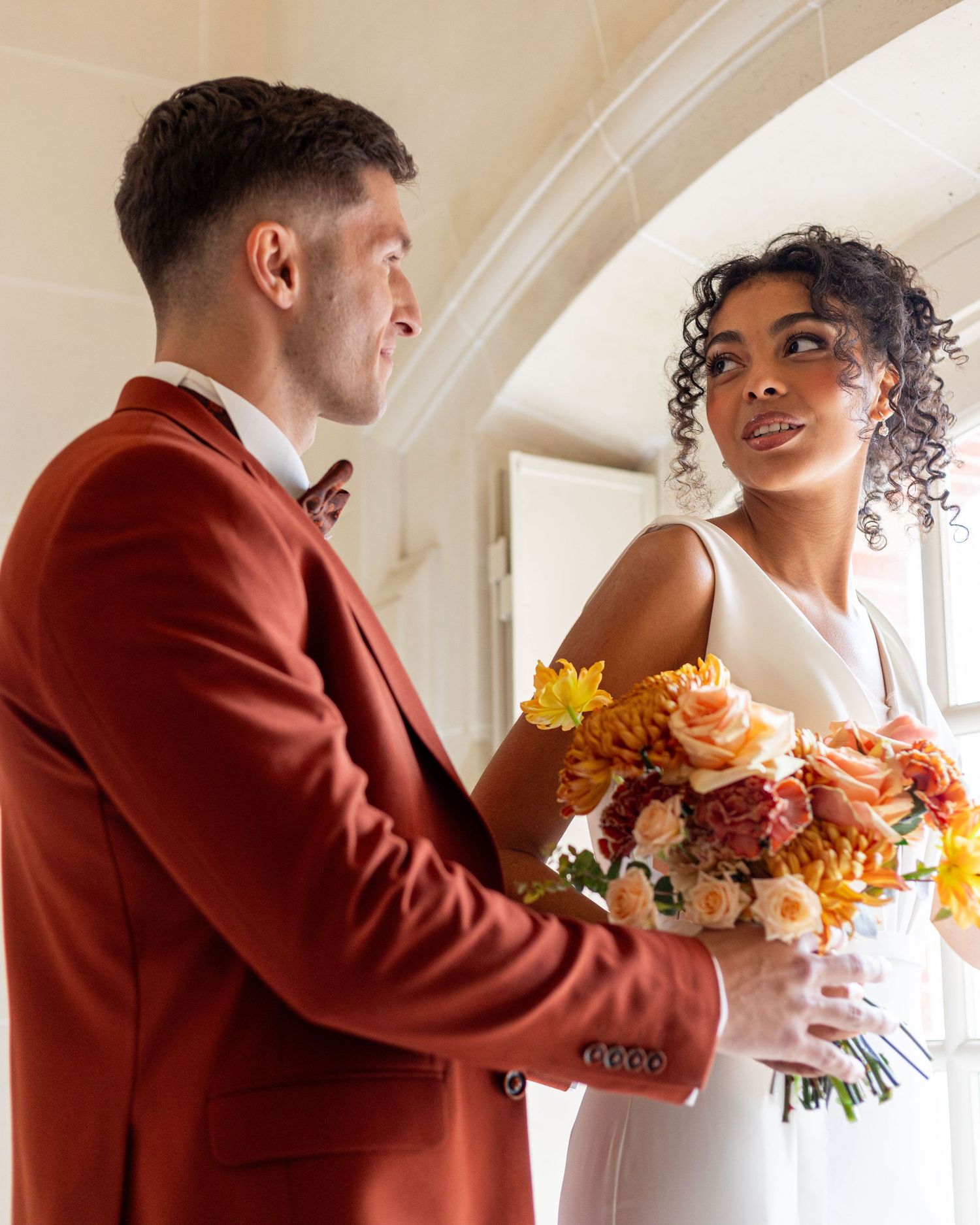 Wedding couple with autumn flowers embracing in elegant indoor setting.