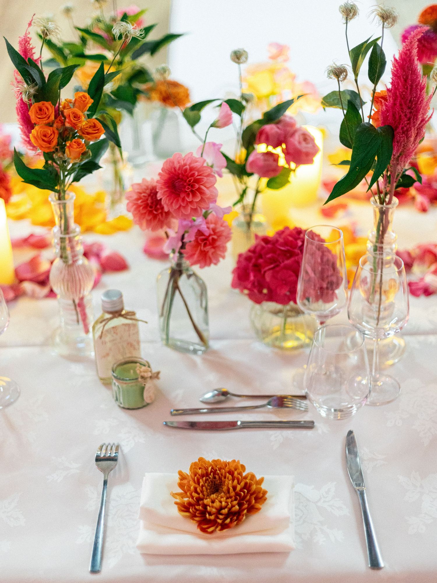 Elegant table setting with pink and orange flowers in small glass vases and place settings.