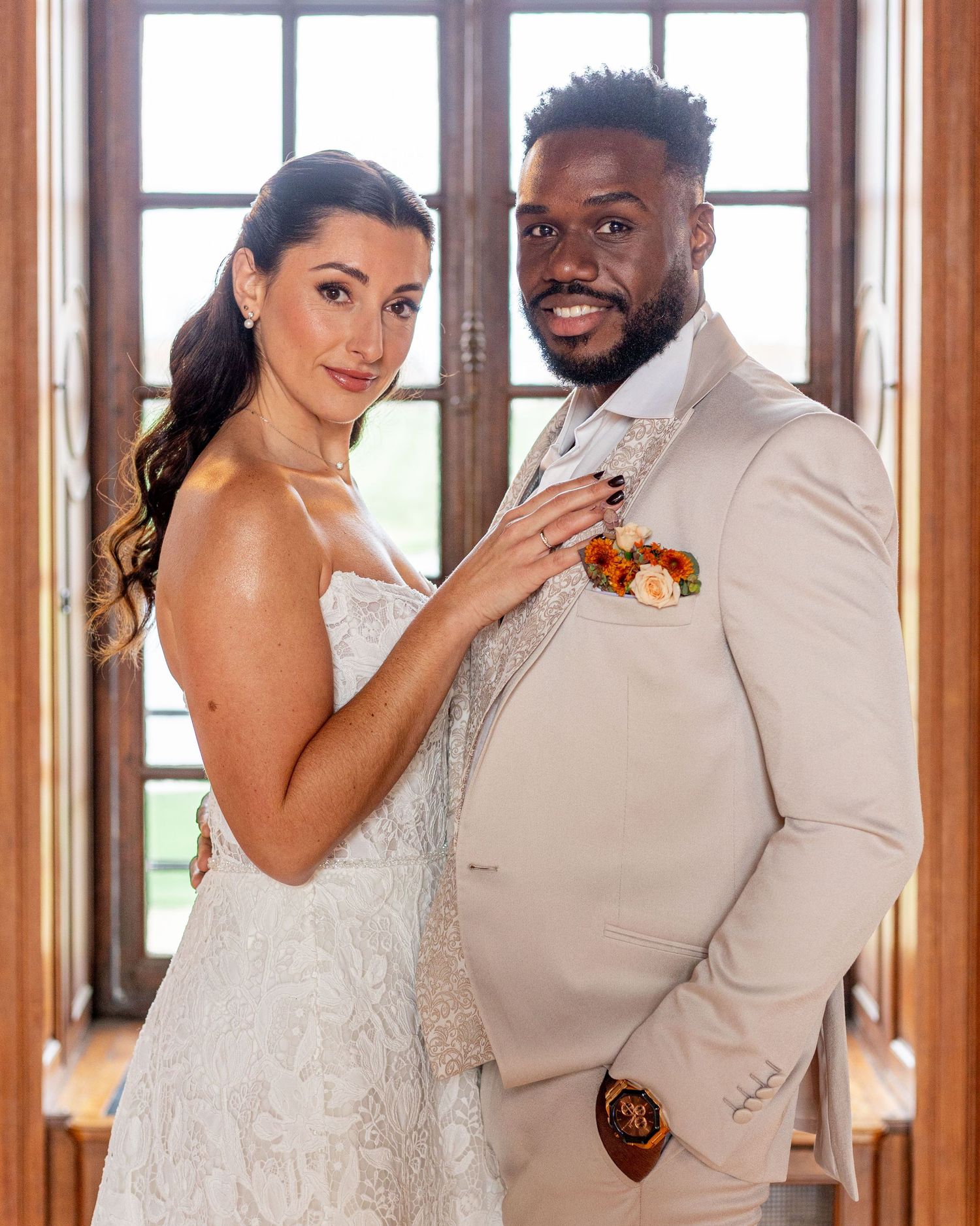 Newlywed couple poses together in elegant venue with wooden window frames.