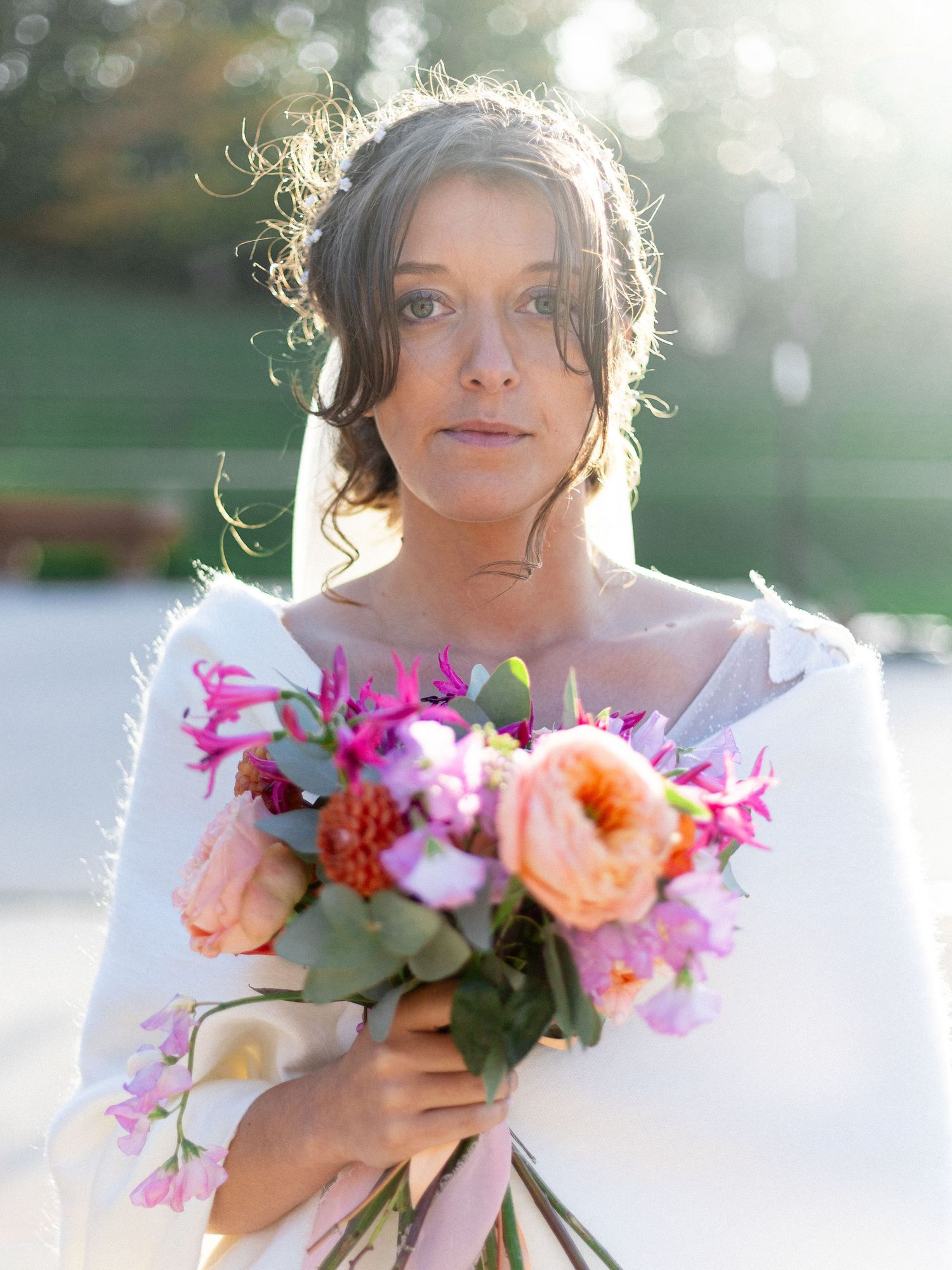 A bridal portrait with vibrant pink and peach floral bouquet in sunlit setting.