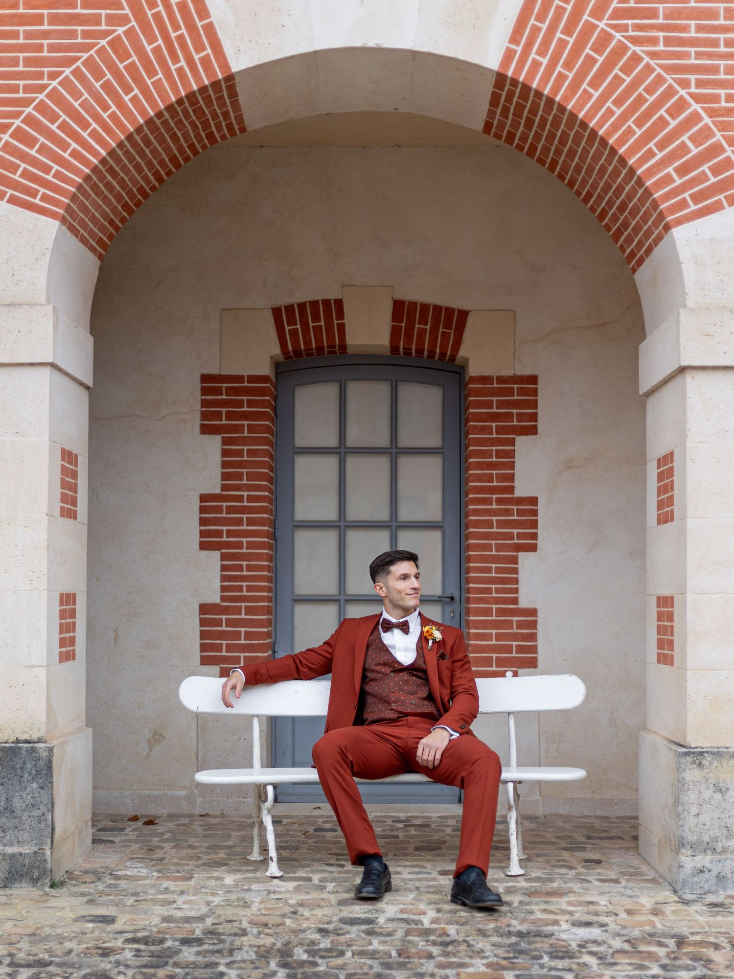 Sequence of architectural shots showing a person in red suit sitting under brick archways.