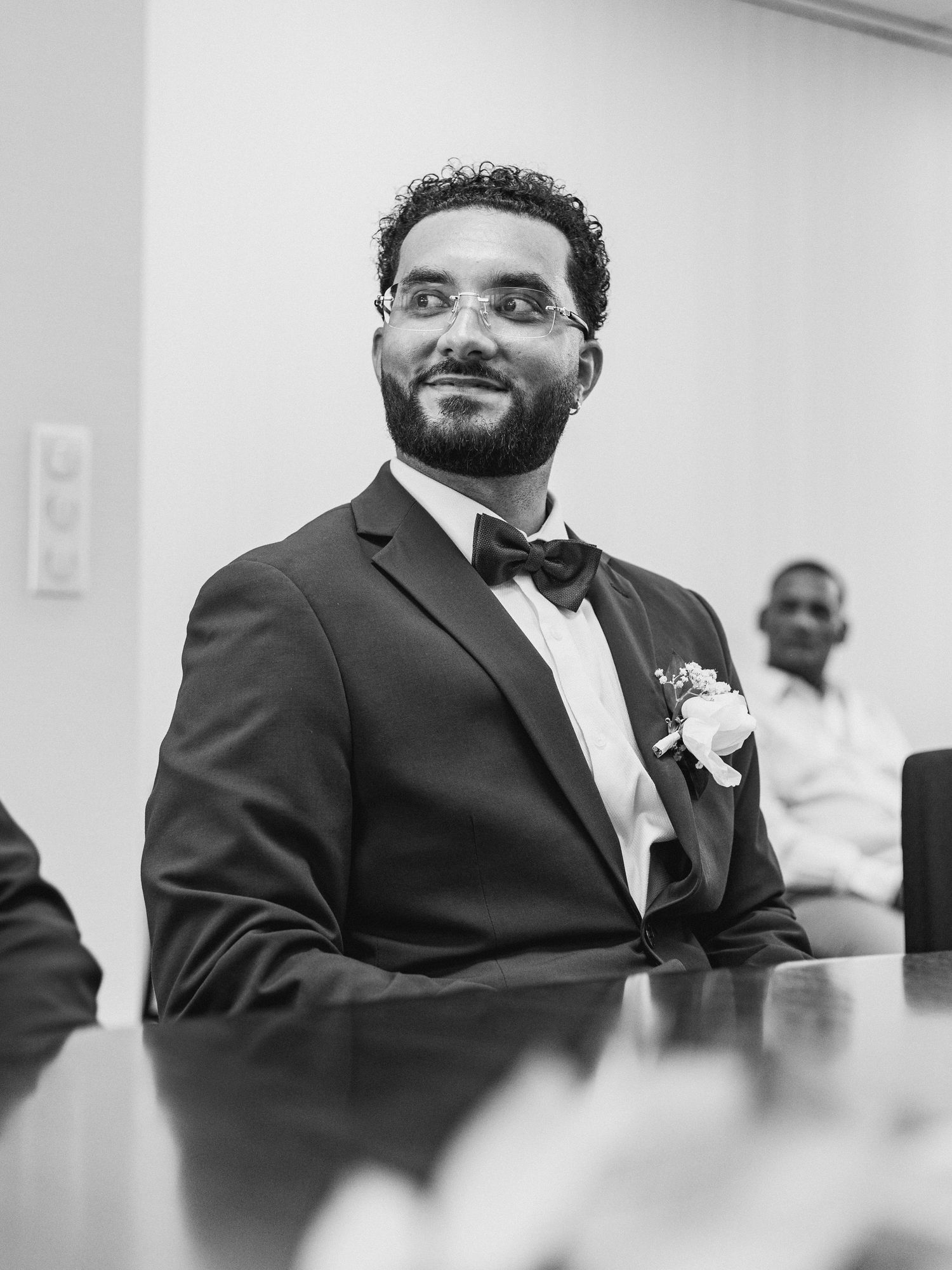 Black and white sequence showing someone in formal attire seated at a conference table.
