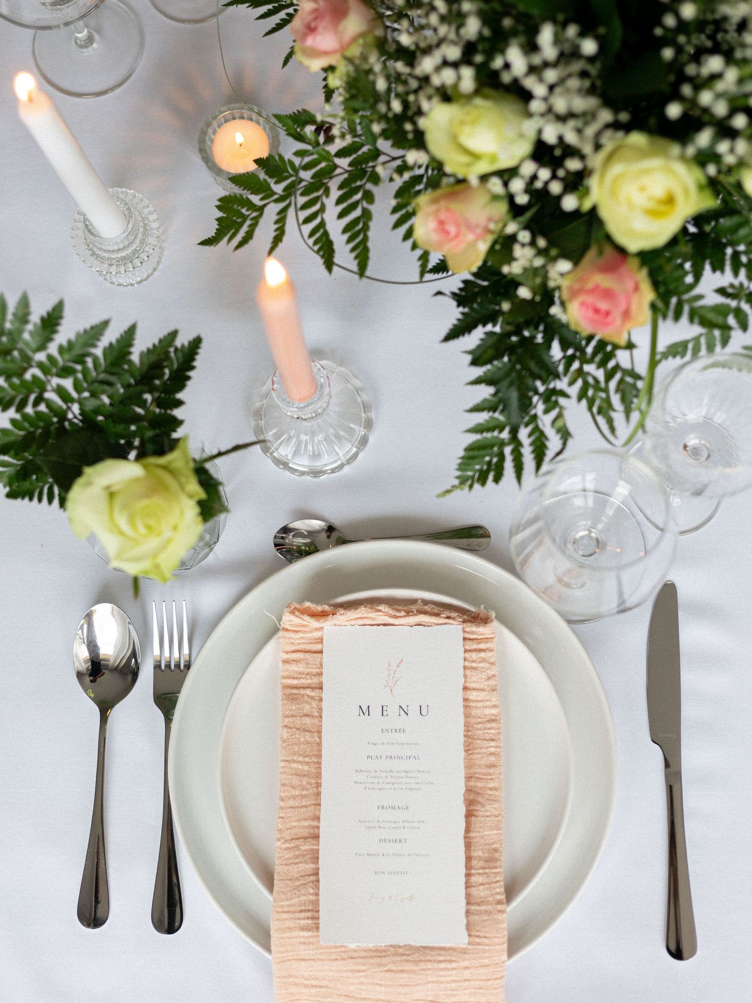 Formal place setting with silverware, crystal glassware, and floral centerpiece in soft peach and white tones.
