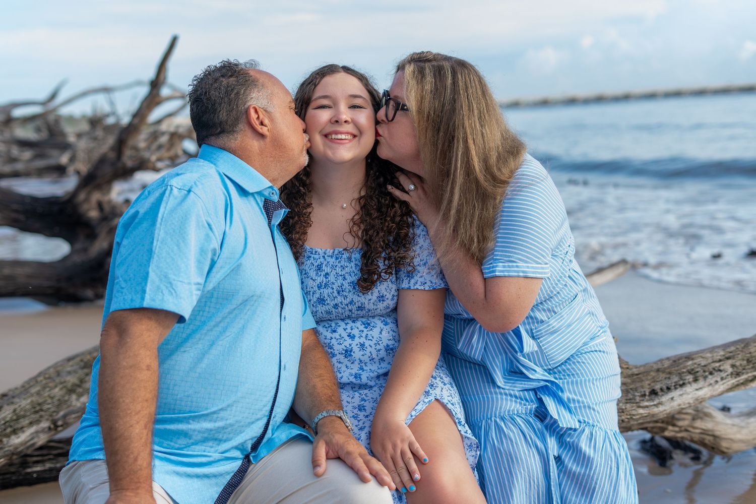A family wearing coordinated blue outfits poses together on a sunny beach for portraits during a photography session.