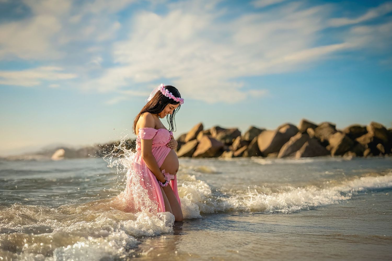 Person in pink dress playing in ocean waves near rocky coastline.