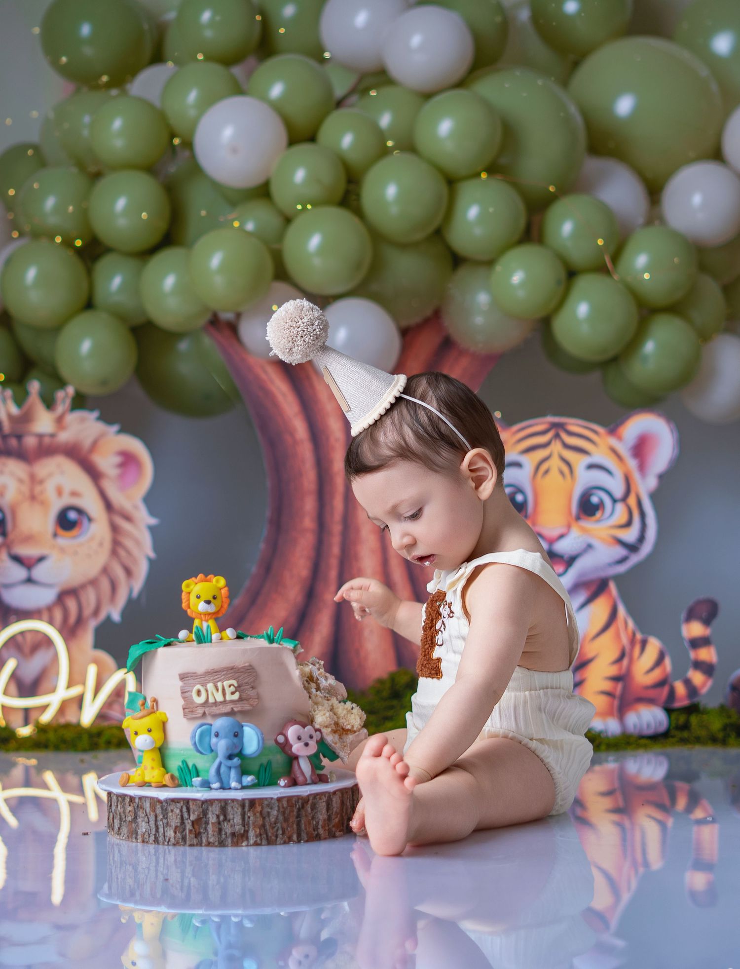 Baby's first birthday cake smash with jungle animal theme, green balloons, and safari decorations.