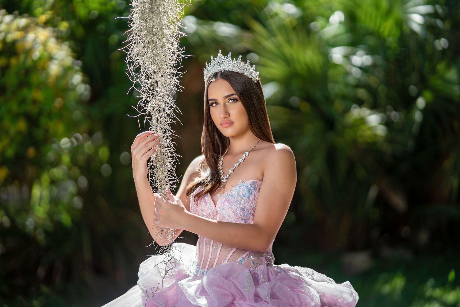 A quinceañera portrait session features a girl in a lavender ballgown posing elegantly in a garden setting.