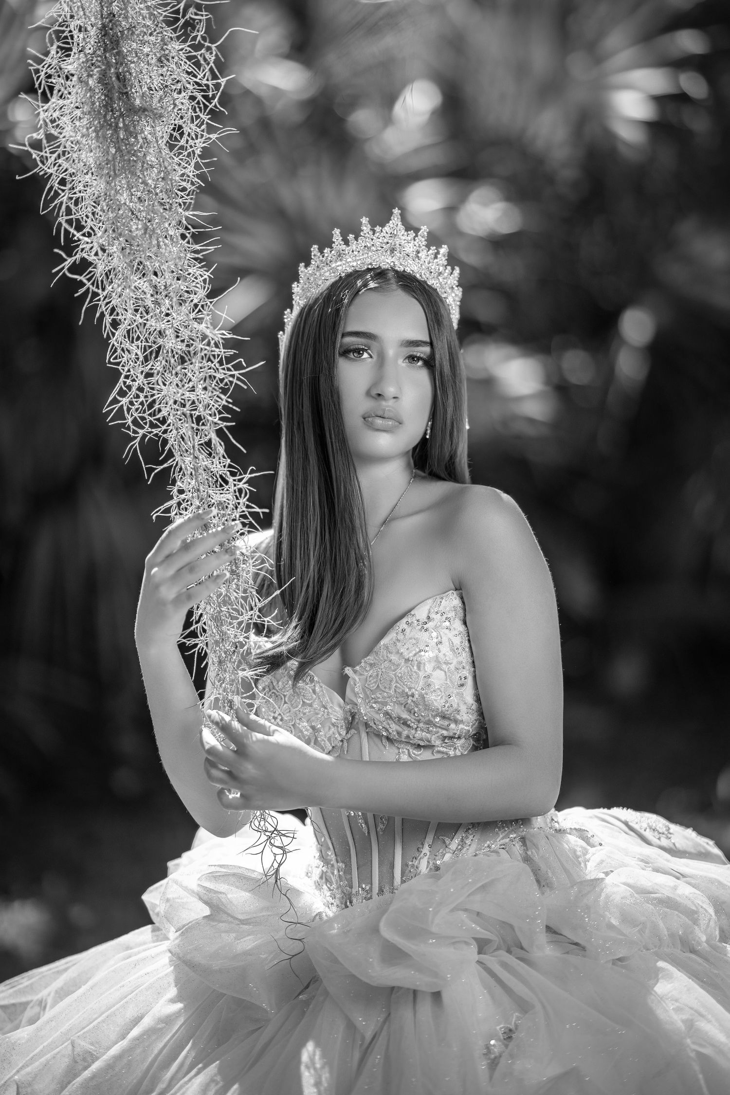 A dramatic black and white portrait showcases an ornate white ballgown and crown against a bokeh background.