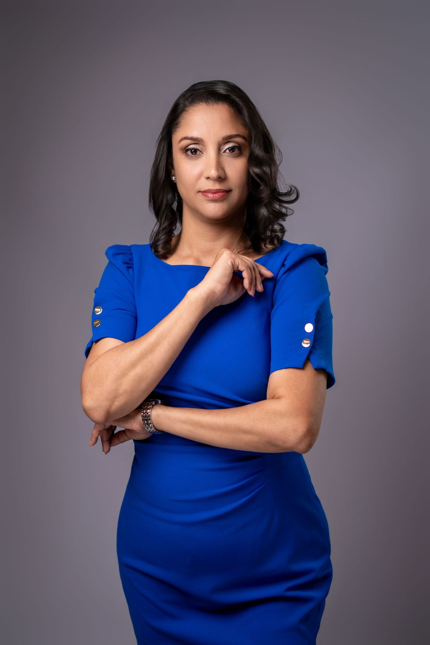 Professional woman in royal blue dress posing confidently against gray background in studio portrait.