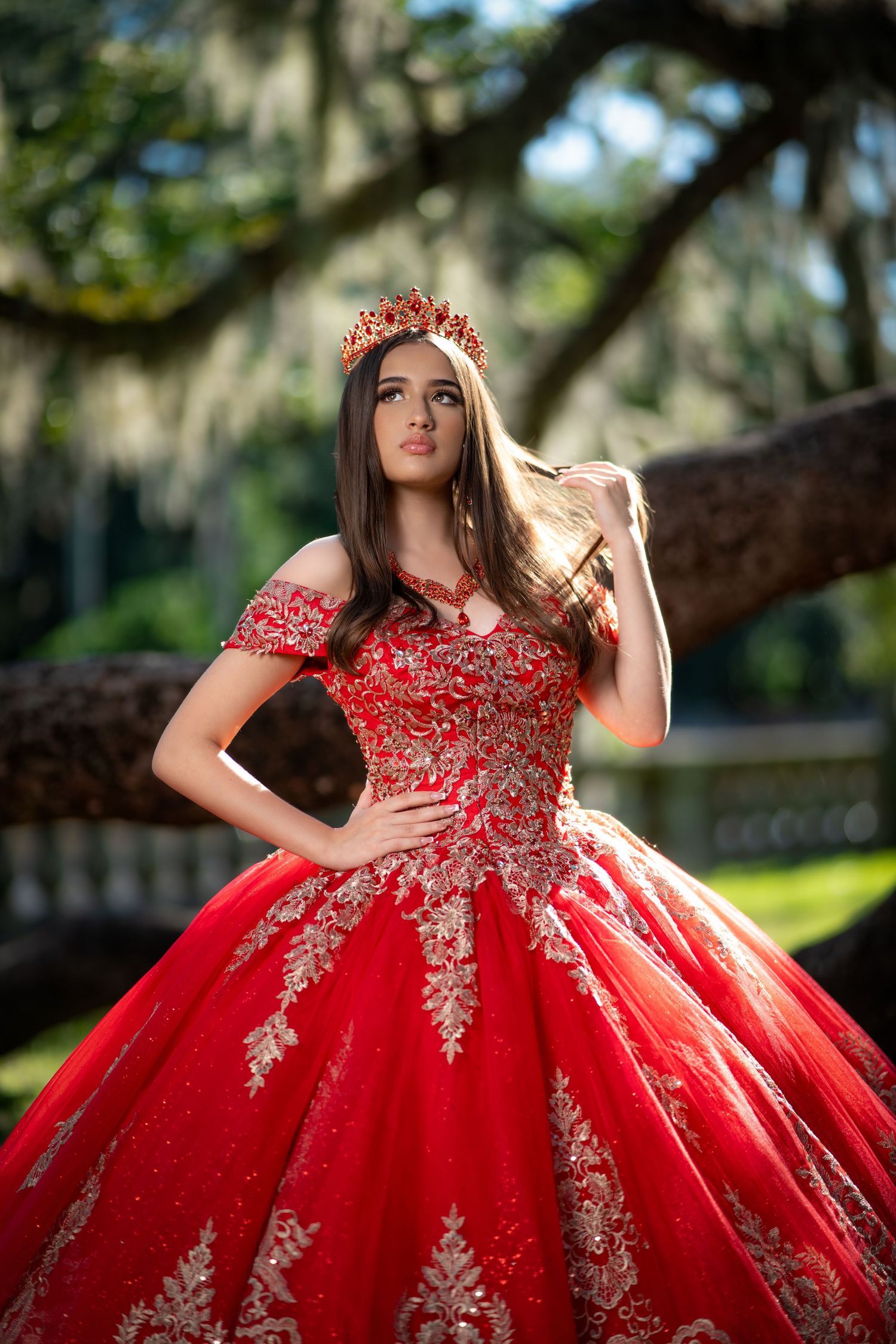 Stunning red quinceañera dress with intricate lace appliques photographed in a garden setting.