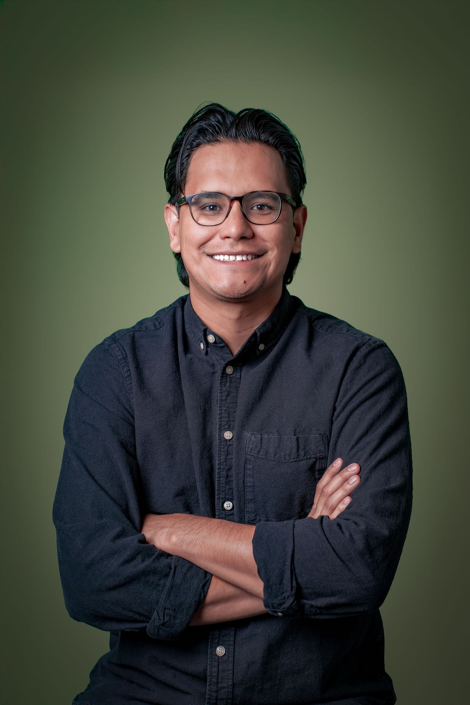 Professional portrait of someone in a black button-down shirt against a green background with warm lighting.