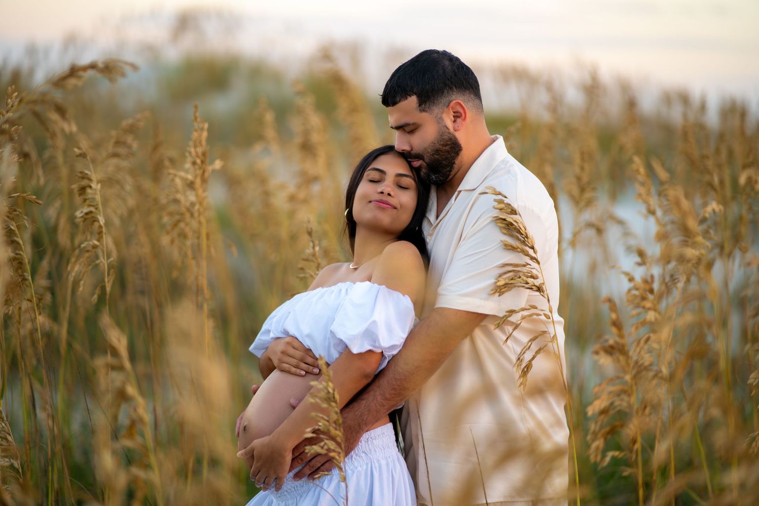 A romantic couple embraces in a sun-lit field of tall grass during golden hour.