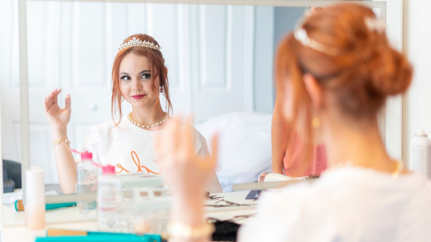 A row of people sit at a bright white counter with beauty products and mirrors in a salon setting.