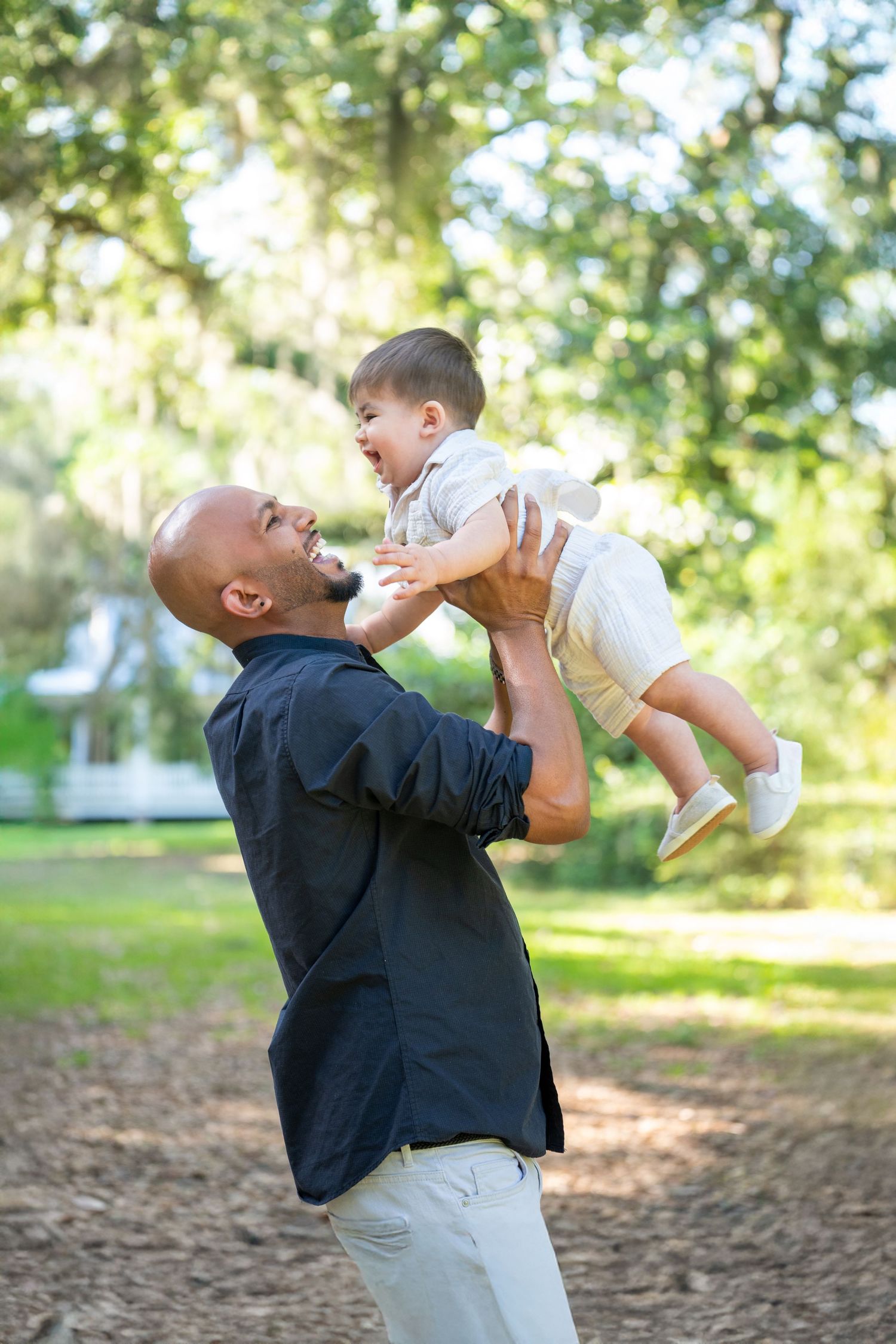 A joyful outdoor moment shows playful interaction between adult and child in a sunlit natural setting.