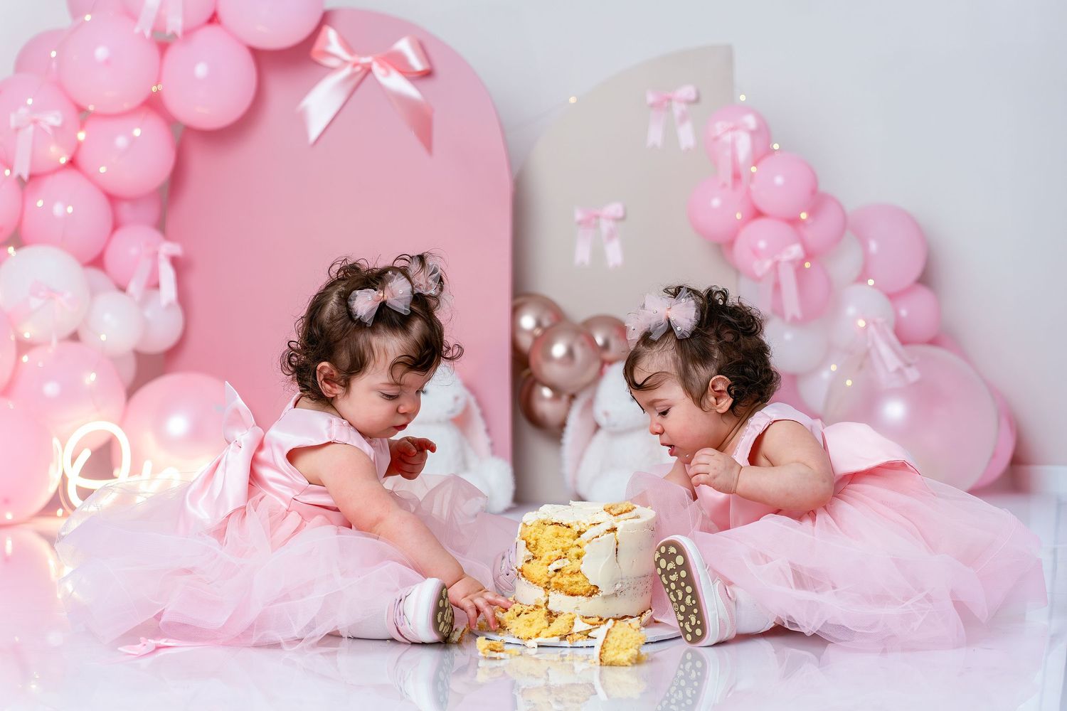 Newborn baby sleeping peacefully on pink background with balloon decorations and soft lighting.