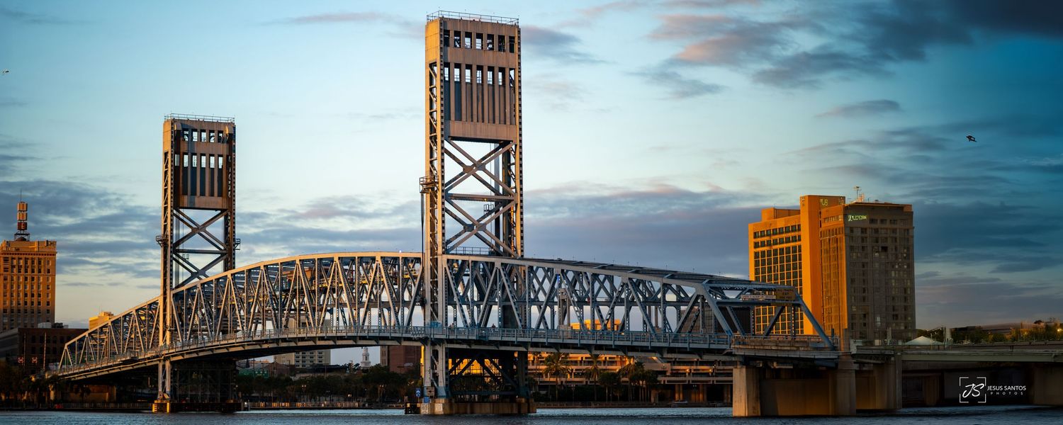 Main Street Bridge spanning St. Johns River with illuminated metal towers against dramatic twilight sky in Jacksonville.