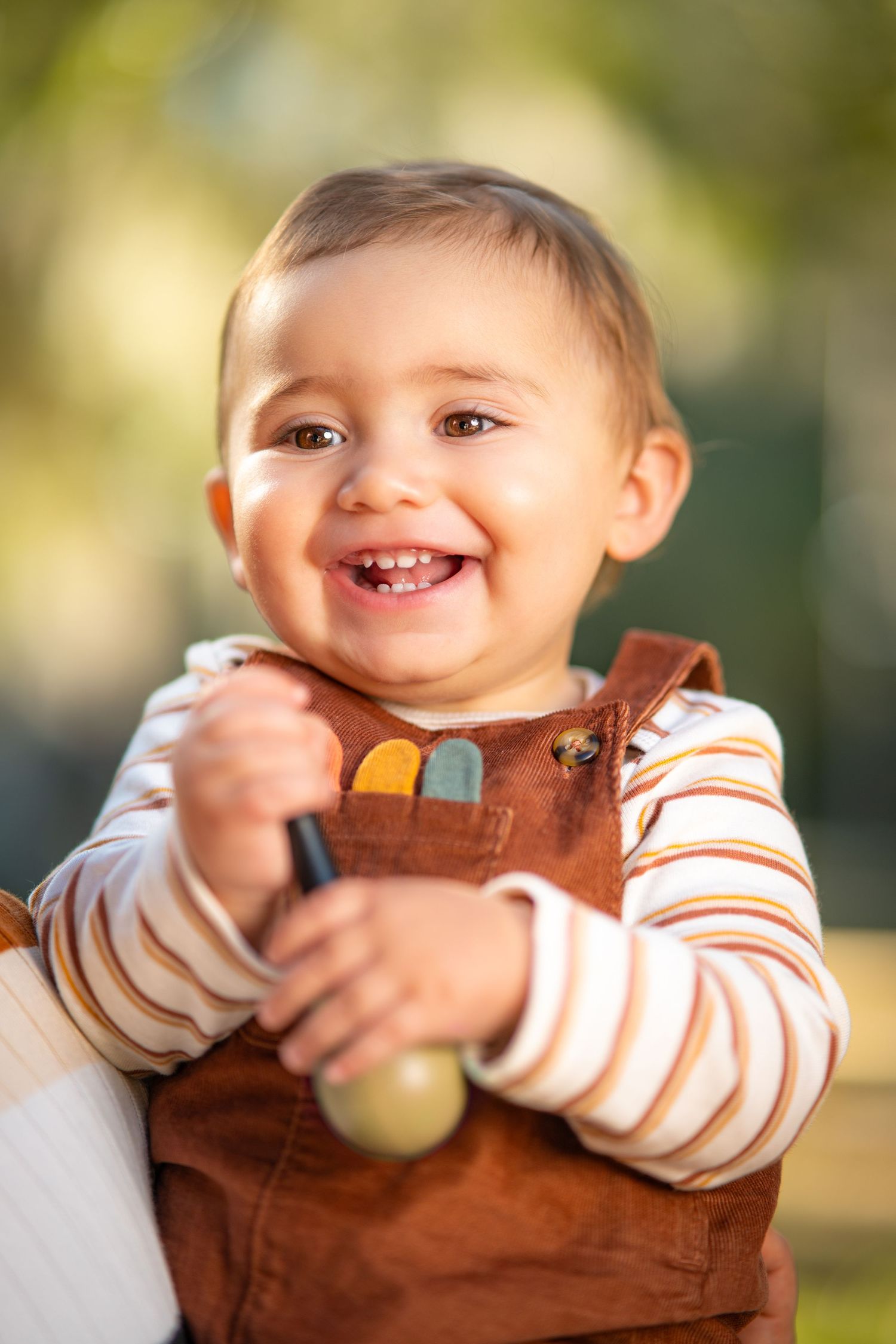 A joyful moment captured in brown overalls and striped shirt against a soft blurred background.
