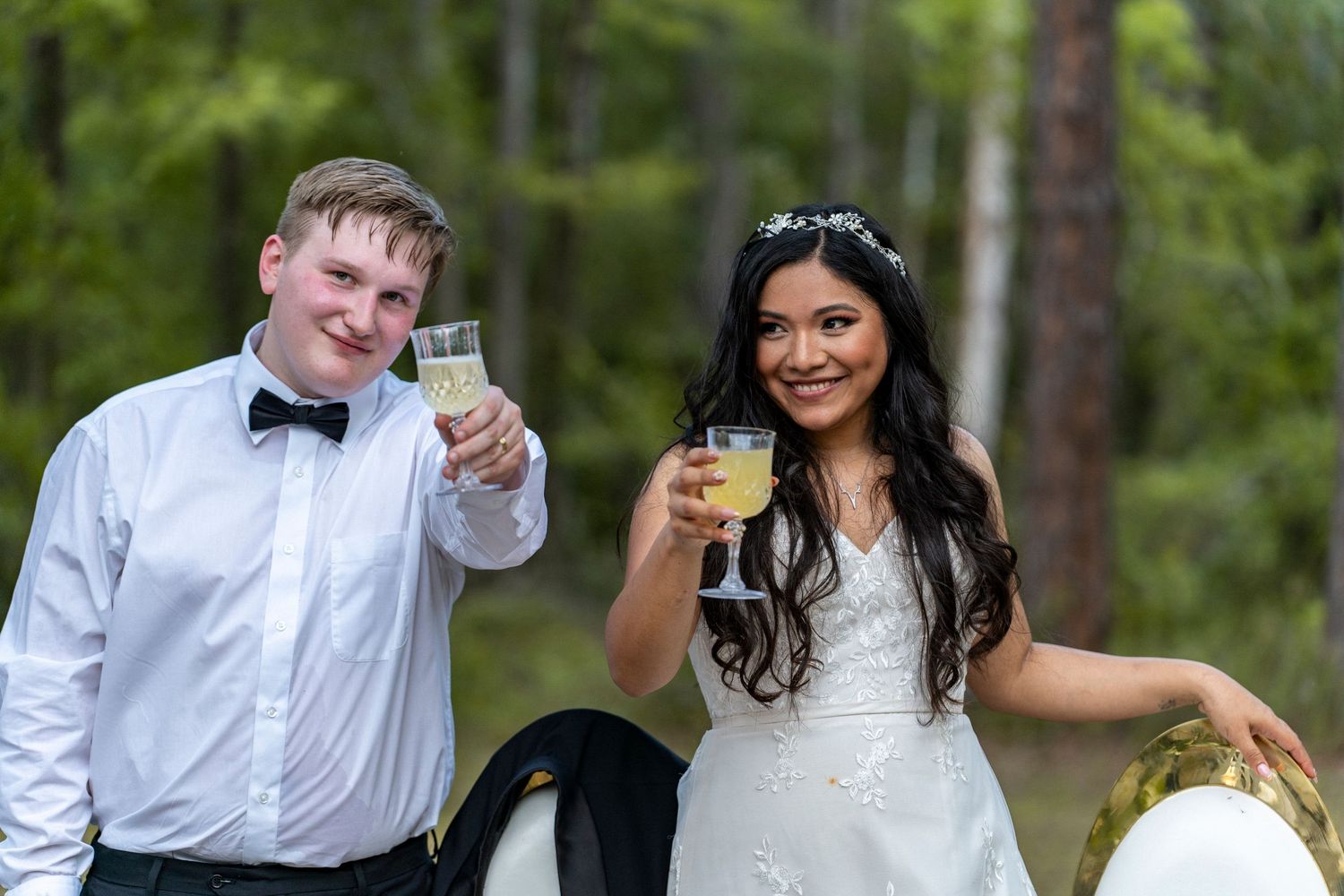 Bride and groom toasting with champagne glasses outdoors in a forest setting on their wedding day.