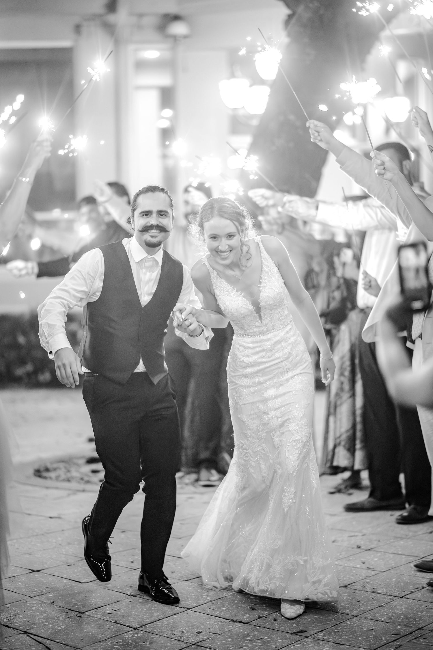 Black and white photo sequence showing a couple walking together during a celebratory sparkler exit at a wedding reception.