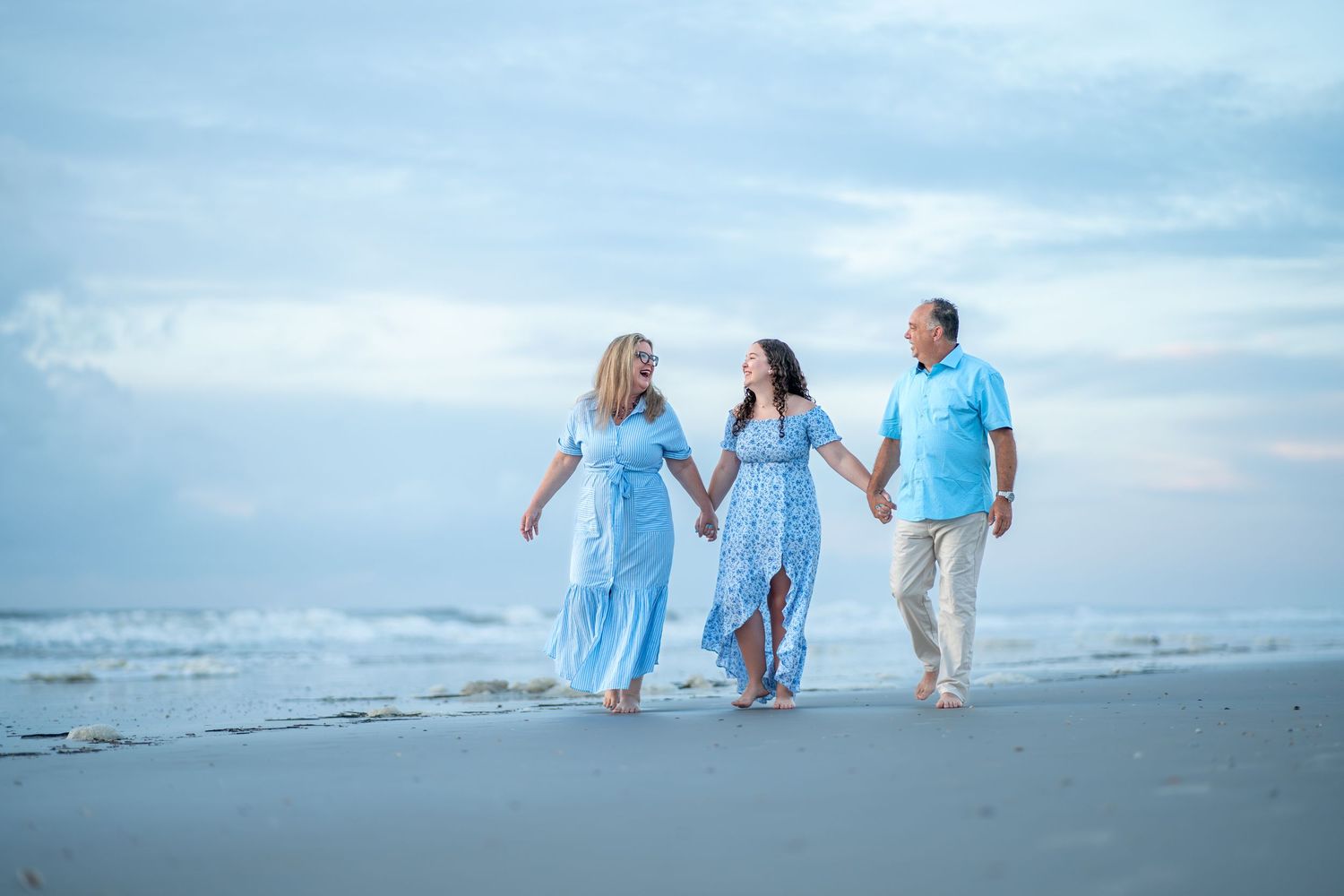 Family members in matching blue outfits walk along the beach during sunset creating beautiful silhouettes.