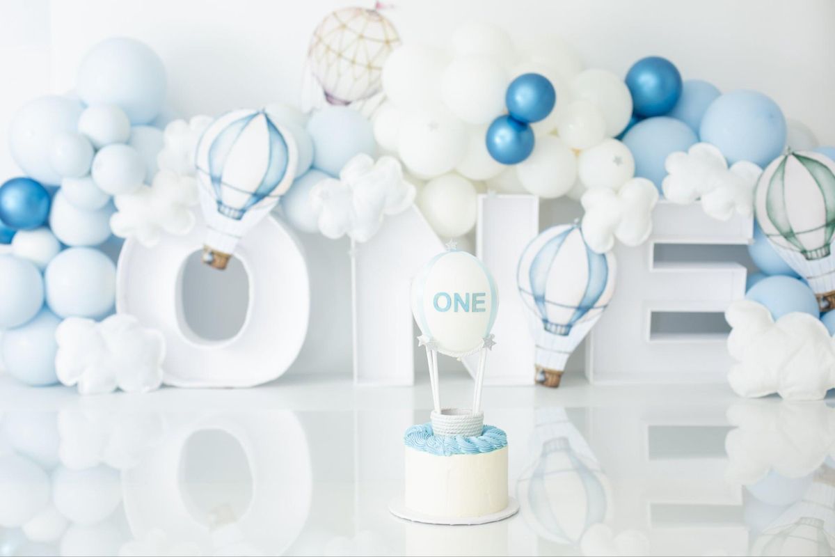 Blue and white balloon arch with ONE letters and hot air balloon decorations for a first birthday celebration.