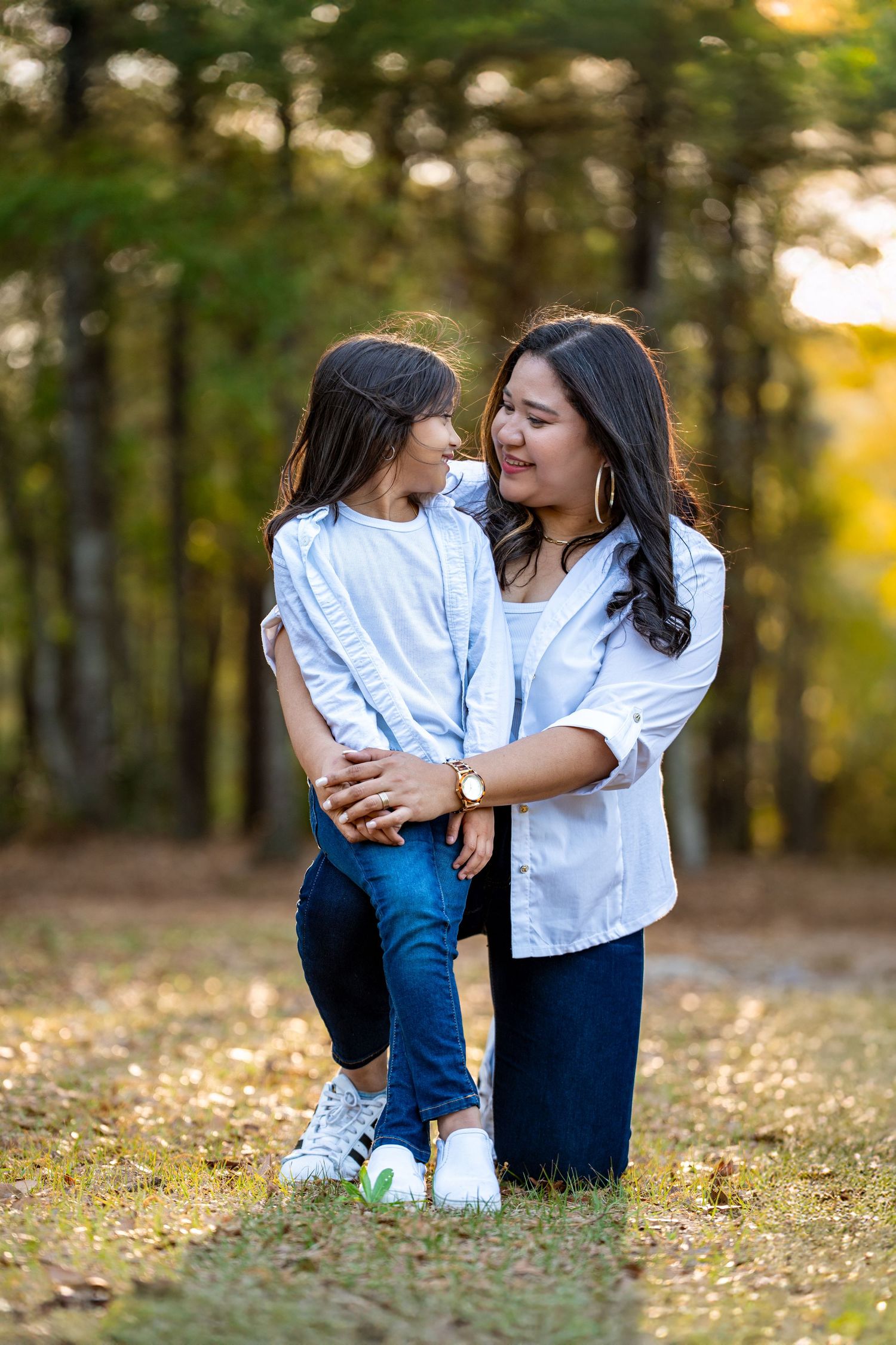 A candid moment between family members sitting in fall foliage during an outdoor photo session at sunset.