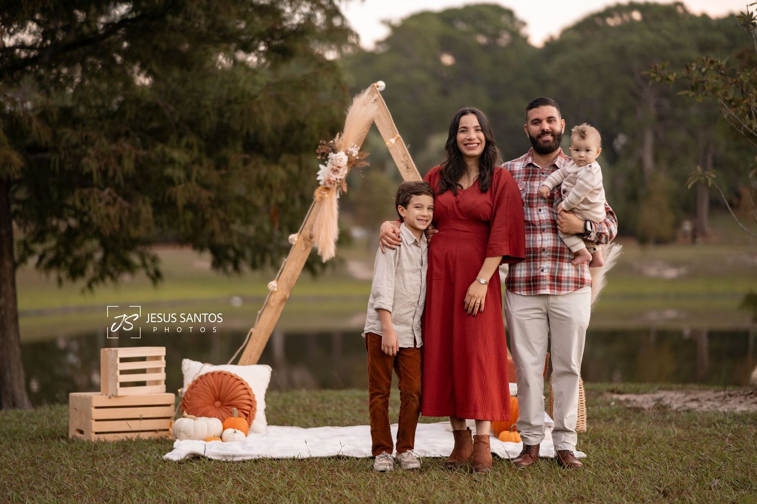 Family wearing coordinated red and white outfits poses together for outdoor autumn photos near a lake at sunset.
