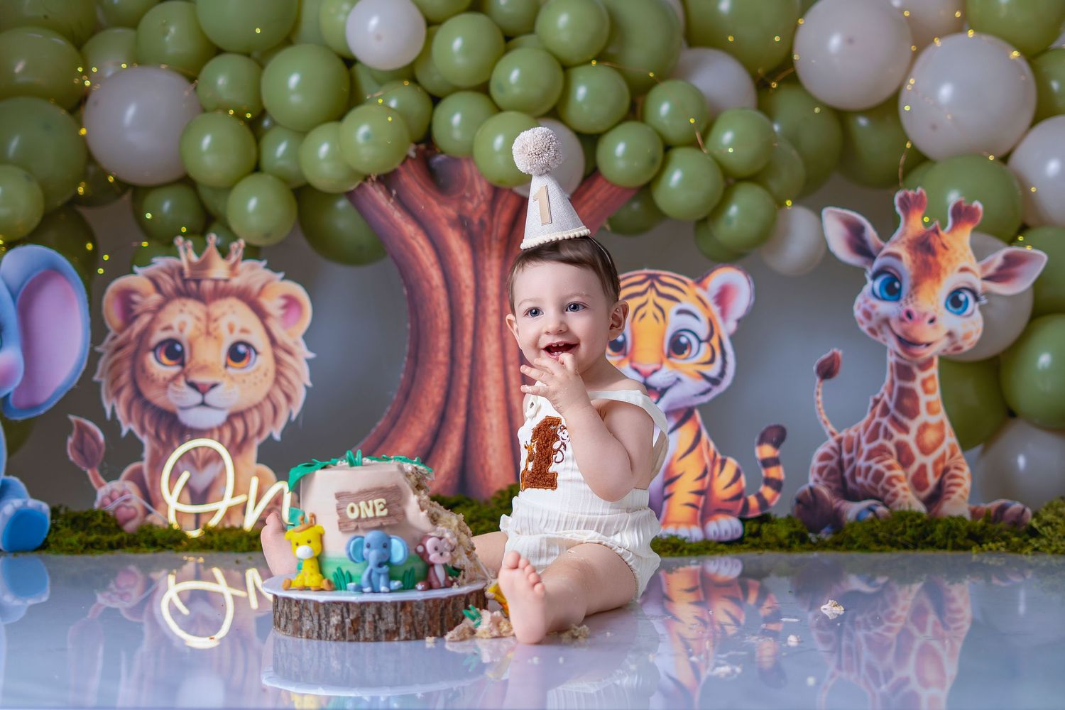 Baby's first birthday cake smash with jungle animal decorations, green balloons, lion, tiger, and giraffe cutouts.