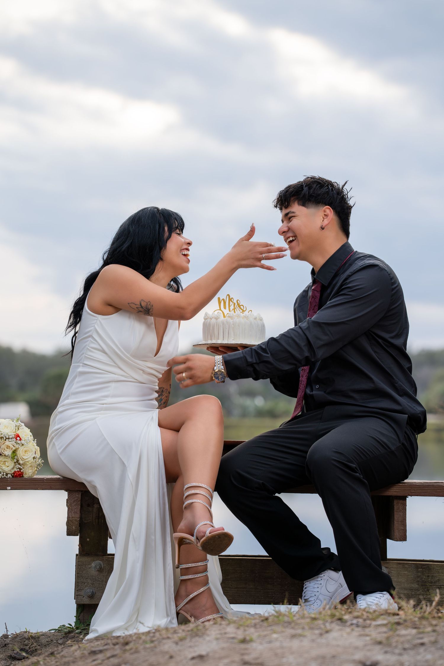 A couple playfully interacting while sitting on a wooden bench by a scenic waterfront.