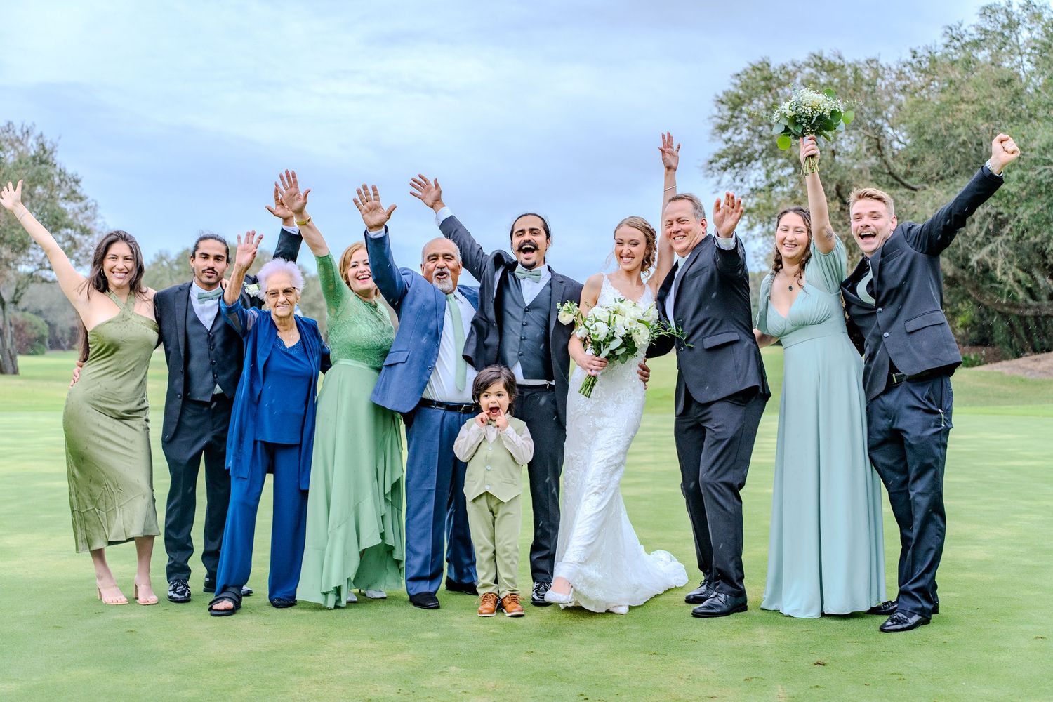 Wedding party celebrating with joyful poses on green lawn.