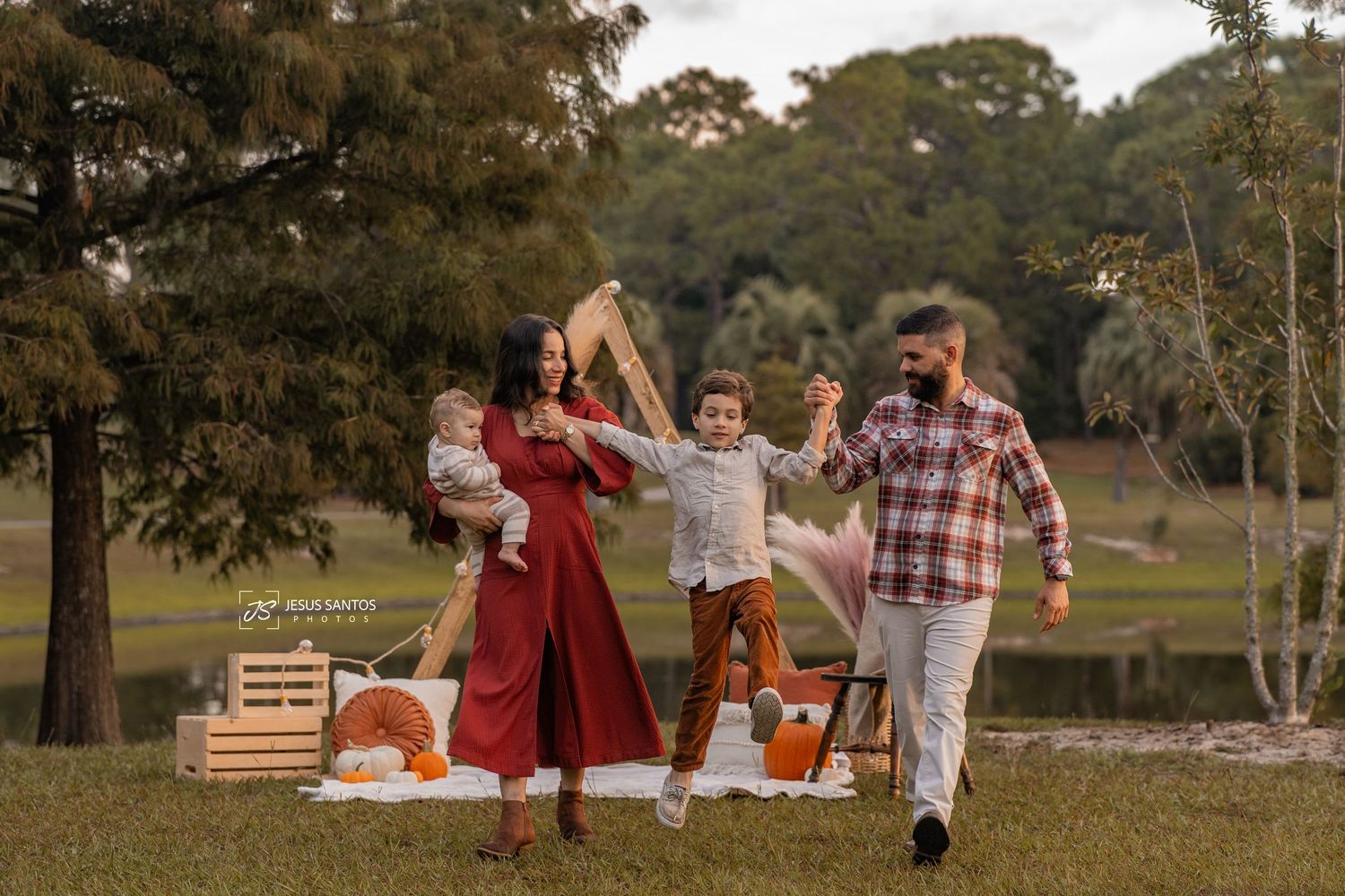 Group enjoying an outdoor autumn picnic with pumpkins and blankets spread on grass near trees at sunset.
