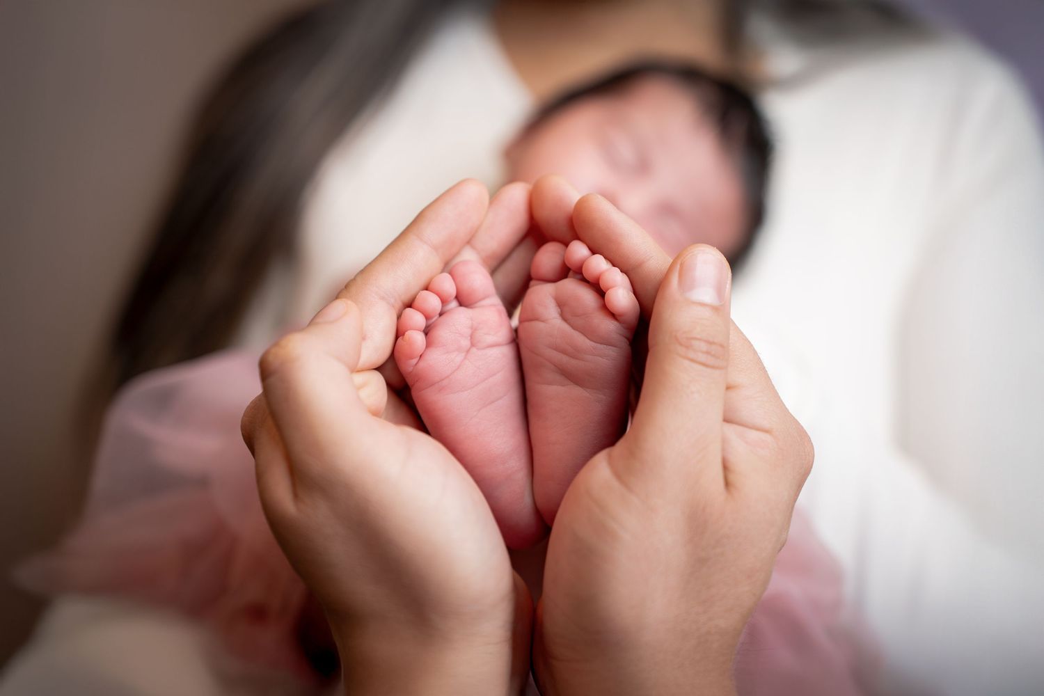 Two hands tenderly hold a newborn baby's tiny feet against a white background.