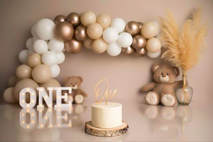 Elegant first birthday party decorations featuring gold and white balloon garlands with 'ONE' lettering and cake display.