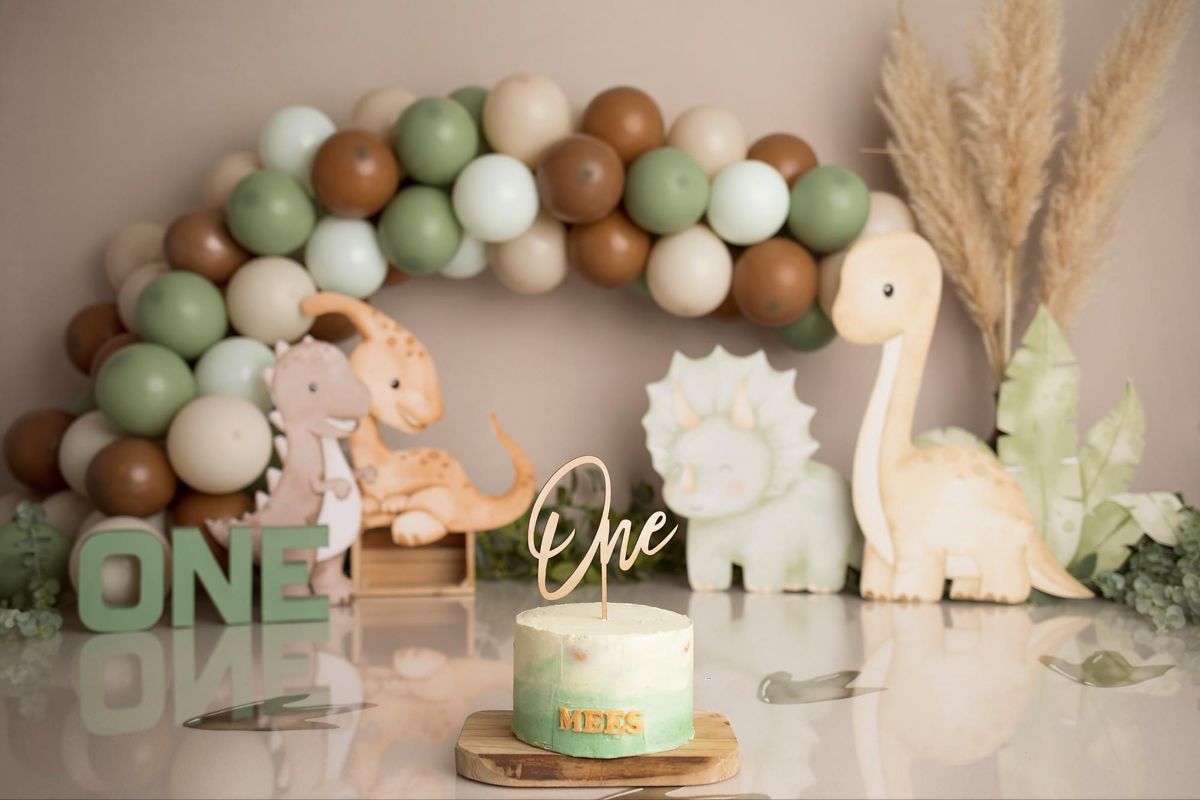 Sage green and brown balloon garland with decorative elements creates an elegant first birthday party backdrop.